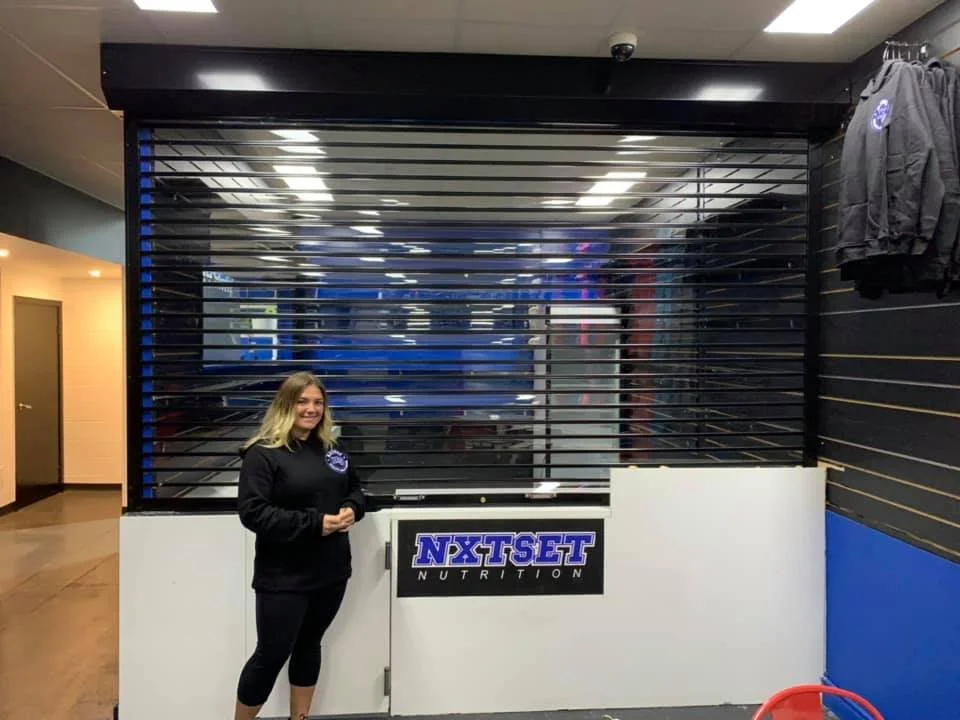 A woman standing inside a closed storefront. The storefront is protected by see through Roller Shutters. Store is in Sydney, Asuatralia.