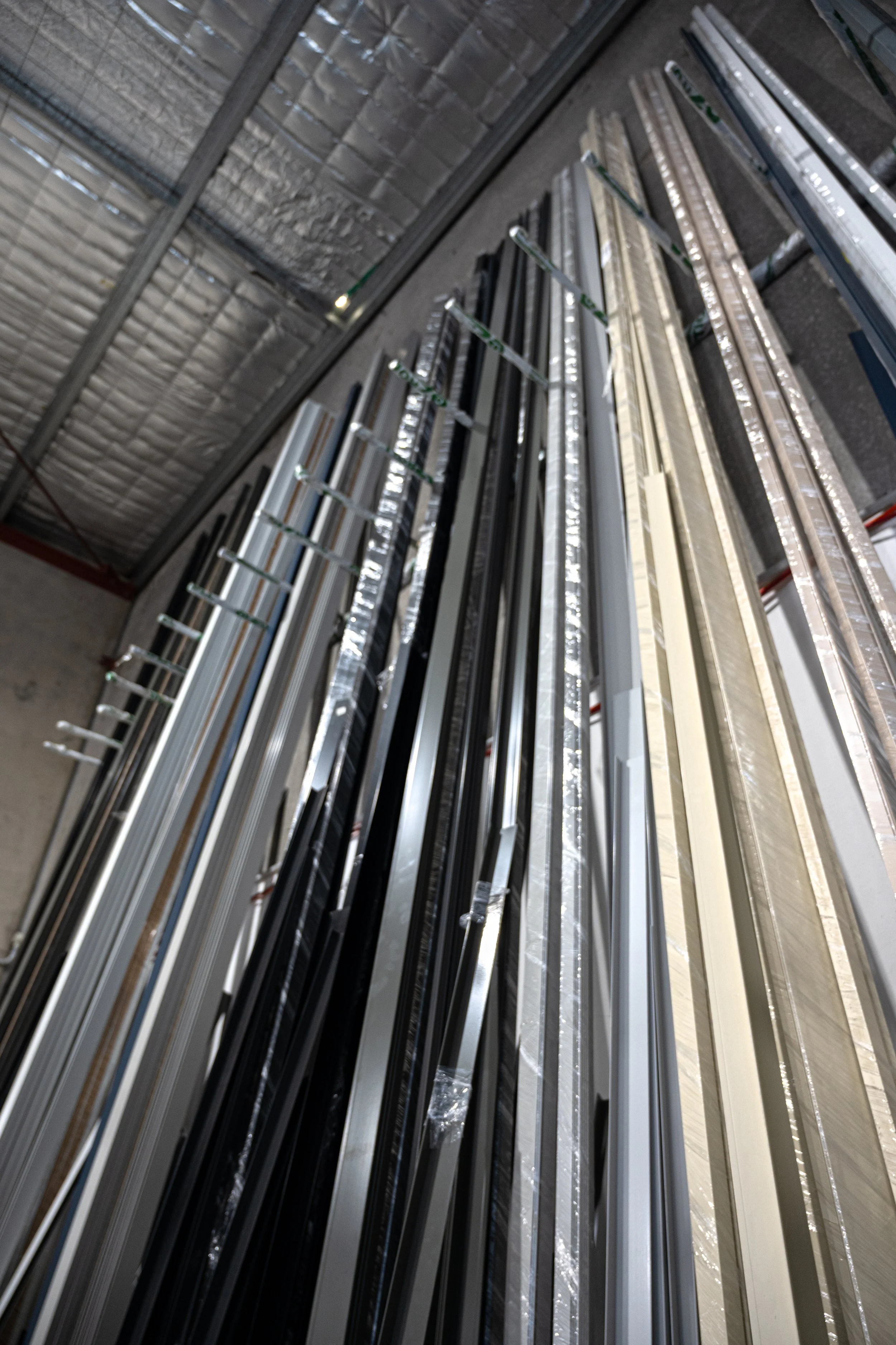 Stacks of metal and plastic window frames or blinds stored vertically in a warehouse in Sydney, NSW.