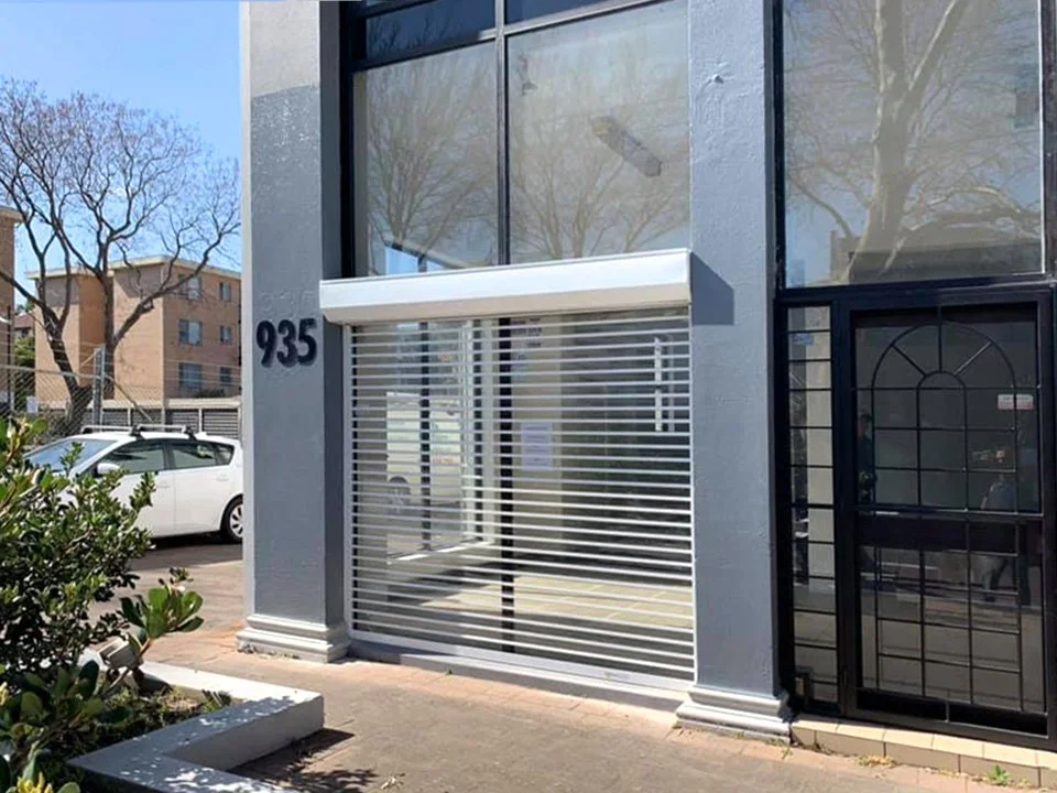 Buildling with a large glass window and metal security shutters, with the address 935 on the wall.