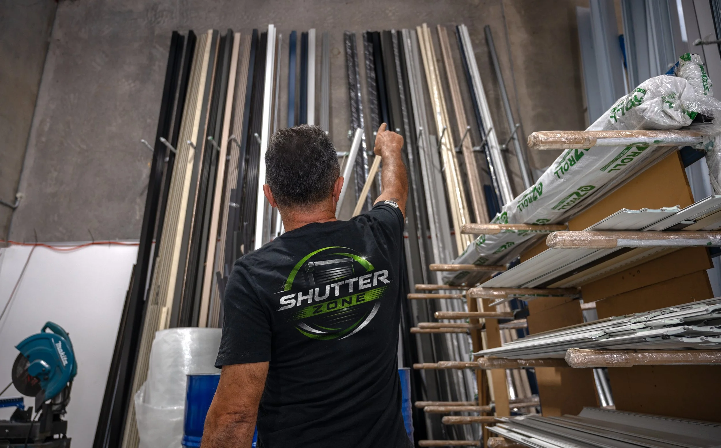 A man pointing at a display of window blinds in a warehouse that sells Roller Shutters.