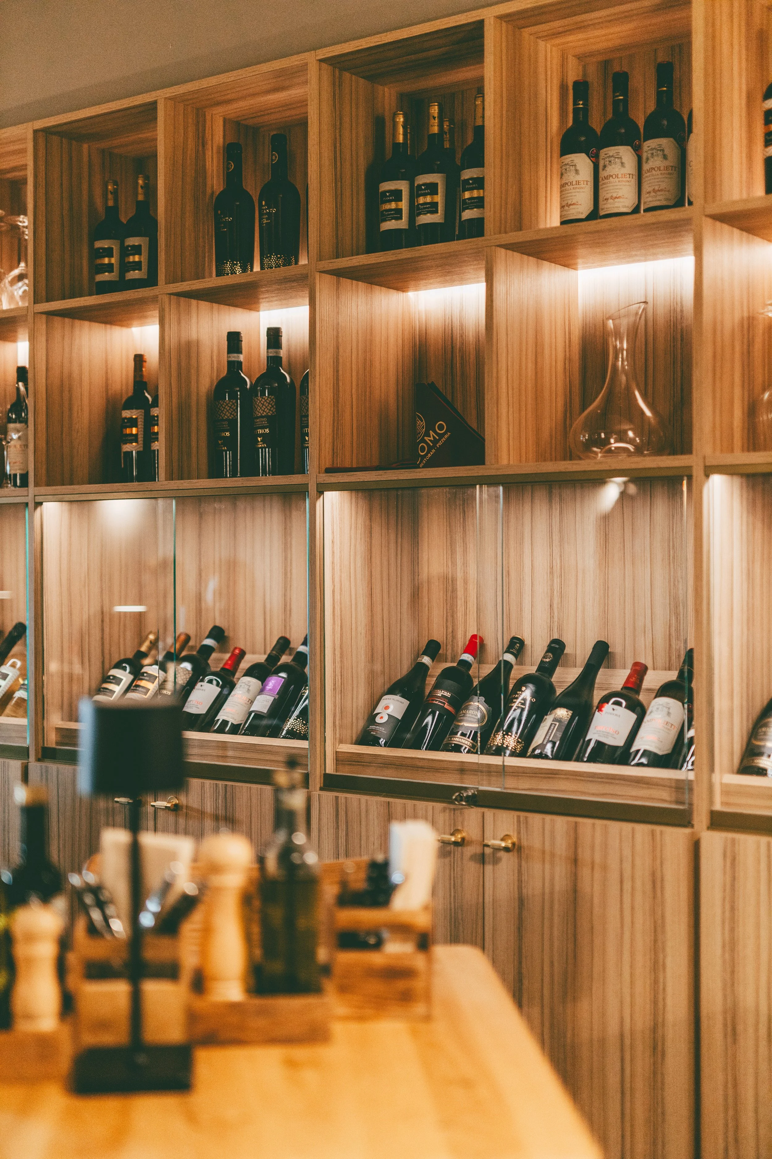 Wooden wine rack store with bottles of wine on display, and a glass decanter on a shelf.