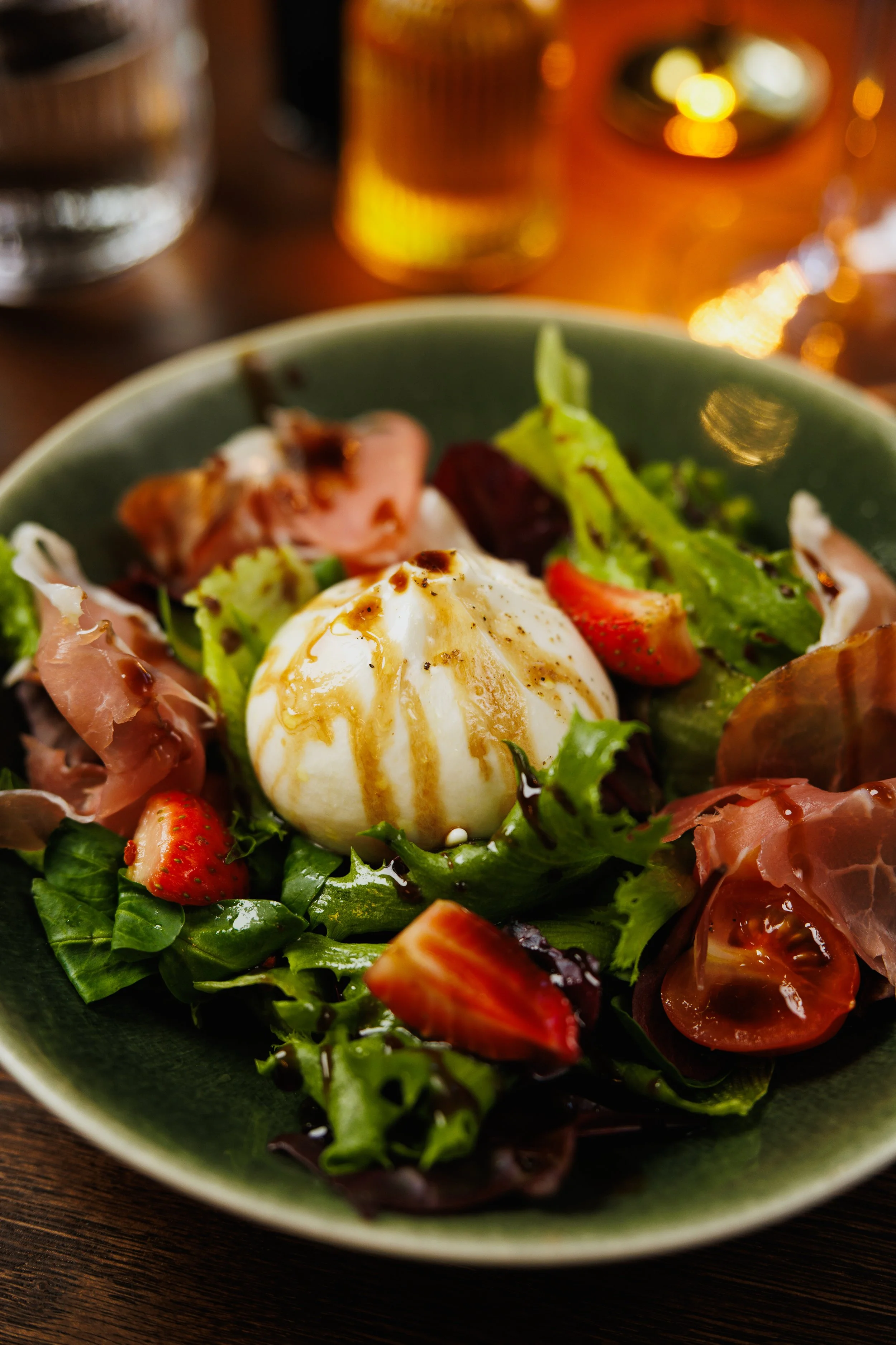 Salad with mixed greens, strawberries, prosciutto, cherry tomatoes, and a soft-boiled egg with dressing.
