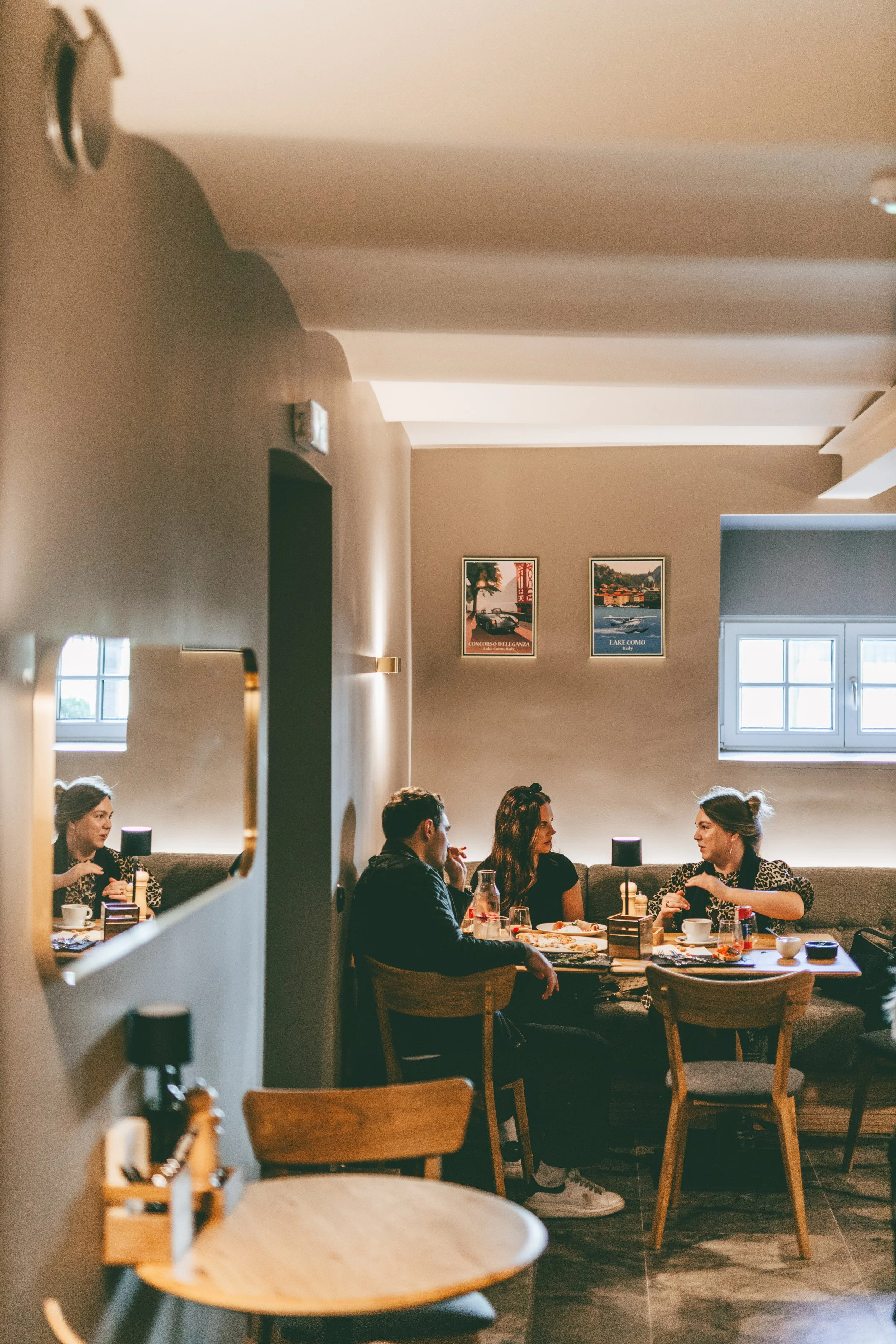 People dining at a restaurant table with food and drinks, engaged in conversation.