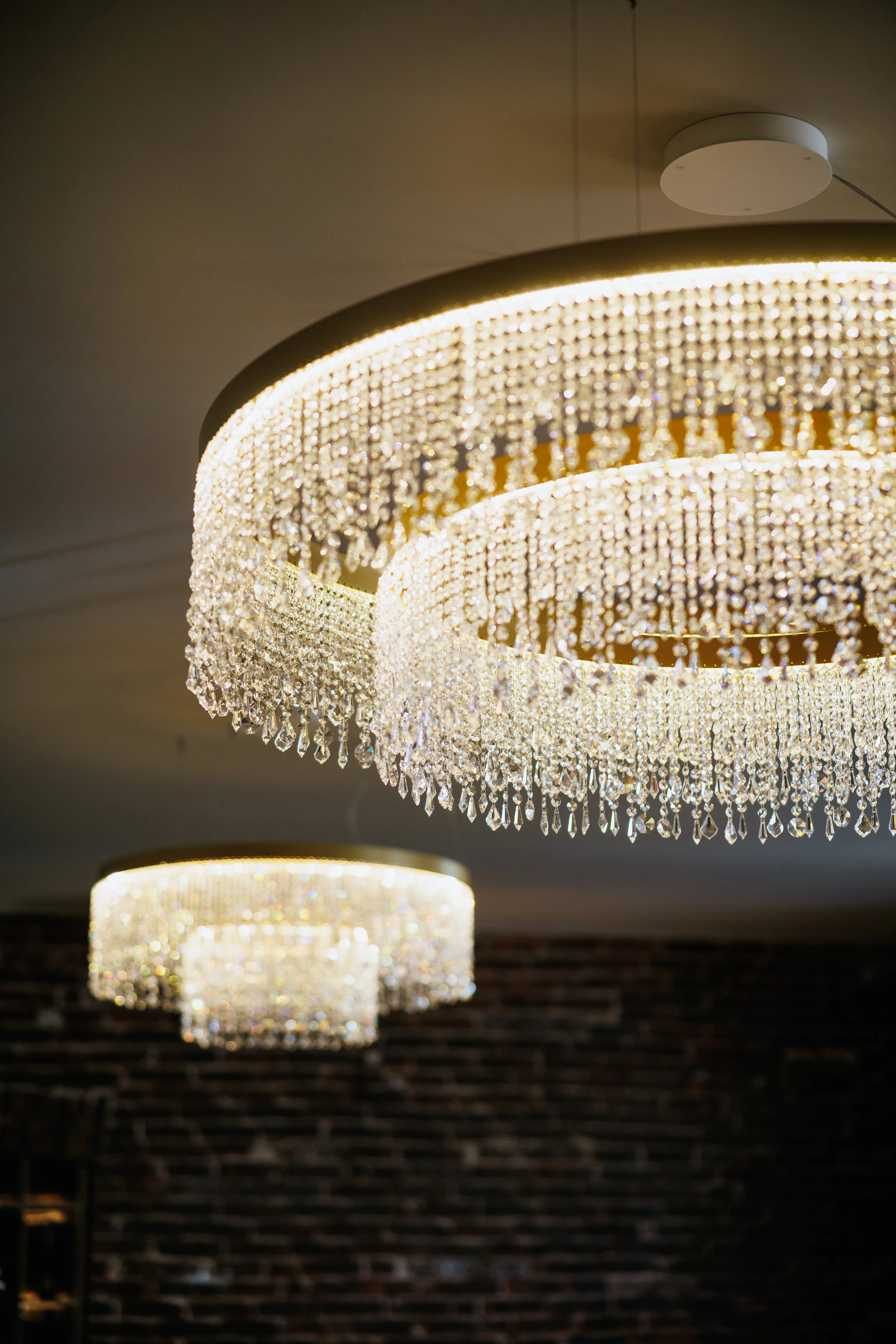 Two elegant chandeliers with multiple tiers of hanging crystals illuminate against a dark background.