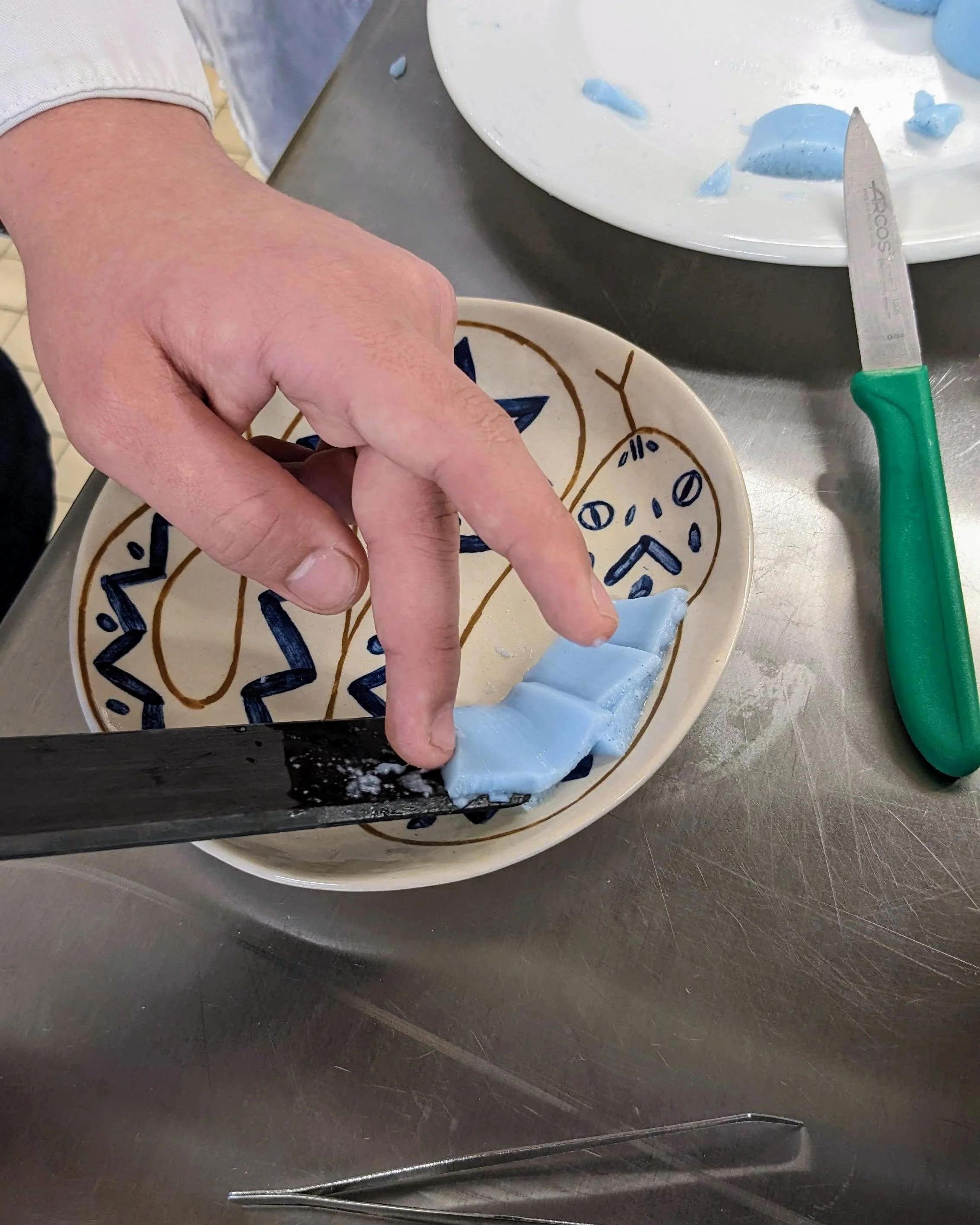Main d'un étudiant déposant une gelée bleue texturée sur une assiette illustrée d'un serpent.