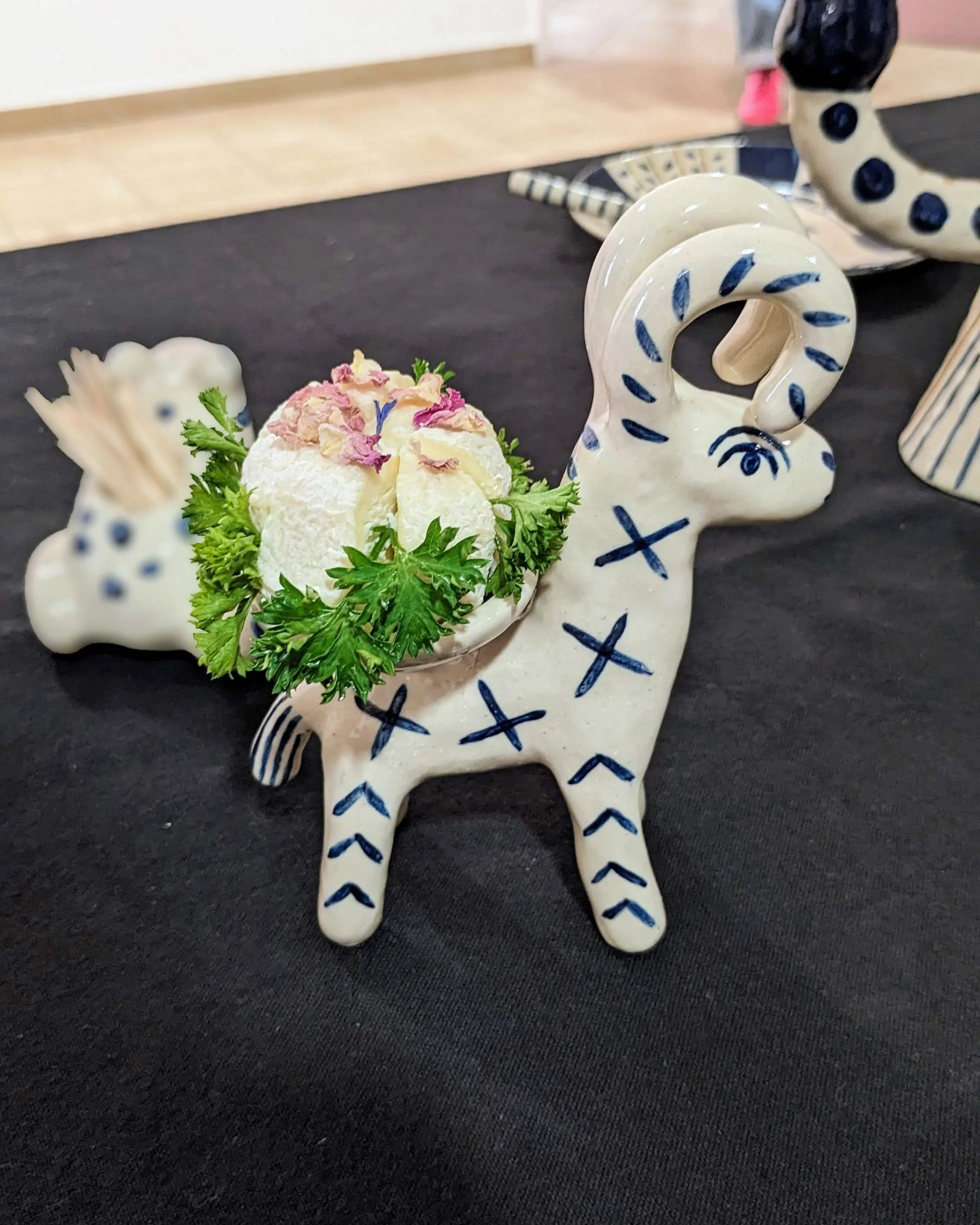 Mise en scène culinaire présentant du fromage de chèvre et du persil sur une céramique en forme de bouquetin.