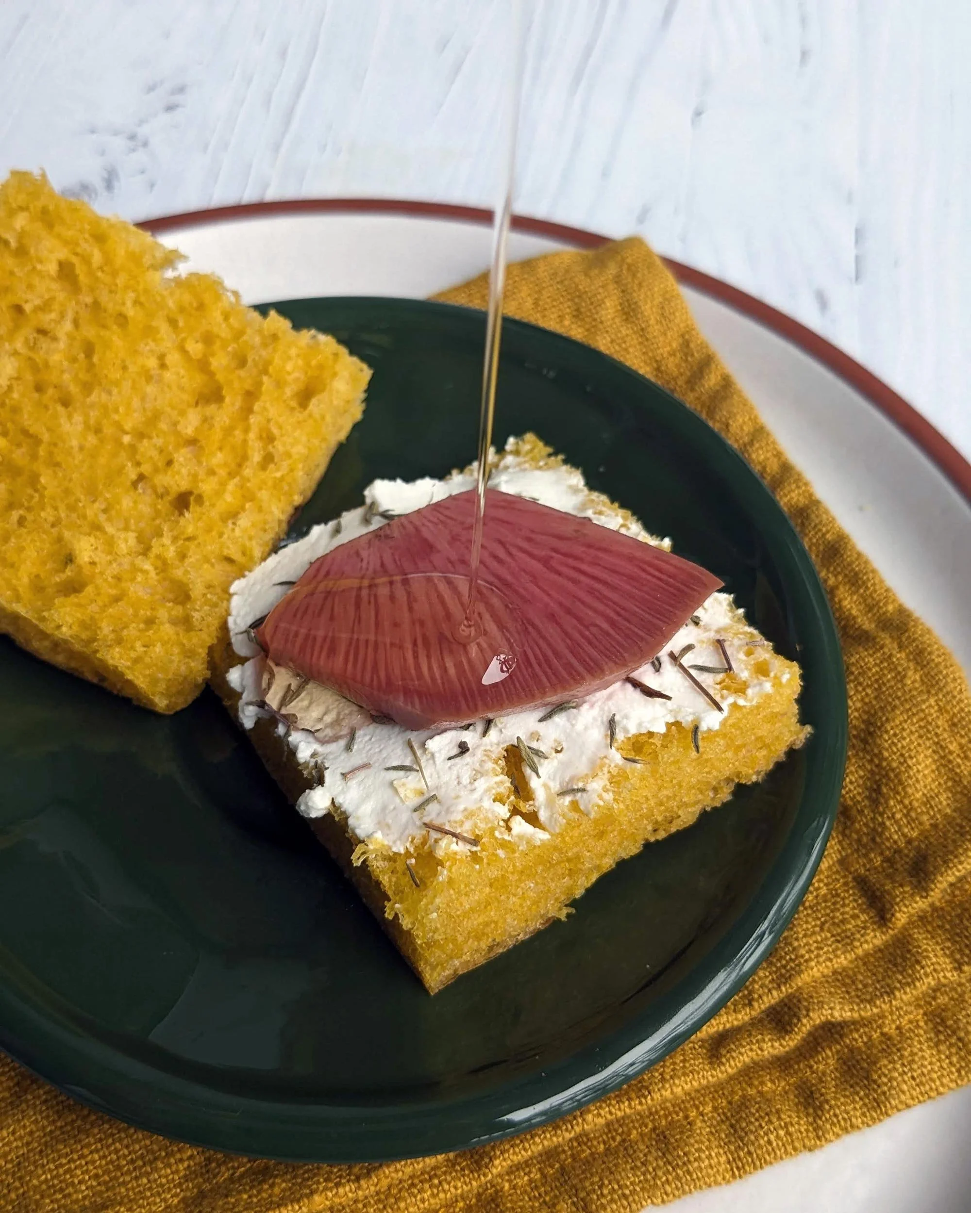 Bouchée de focaccia jaune au curcuma garnie de fromage frais et d'un pickle artisanal.
