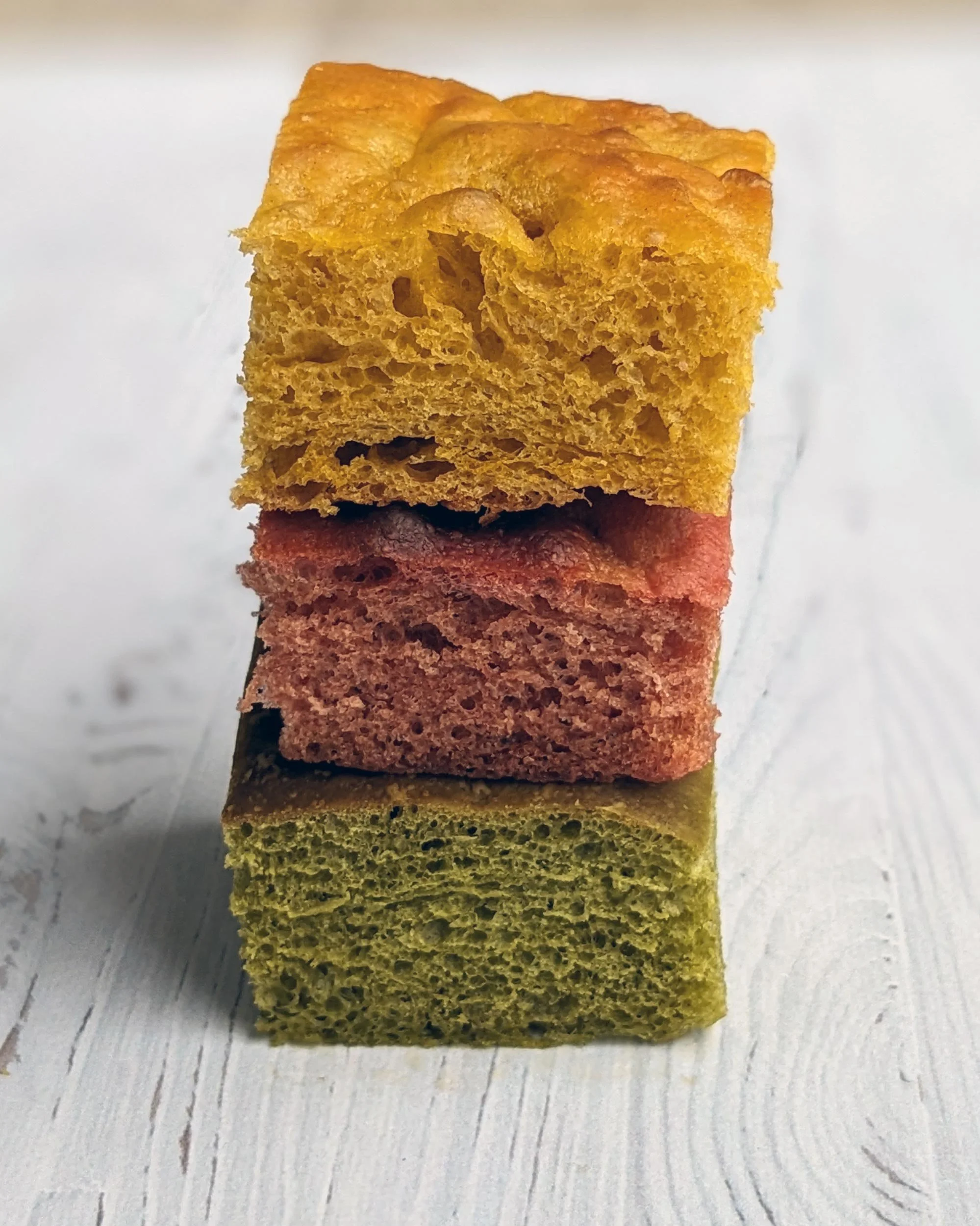 Parts de focaccias colorées naturellement en vert, jaune et orange grâce à des jus de légumes pressés.