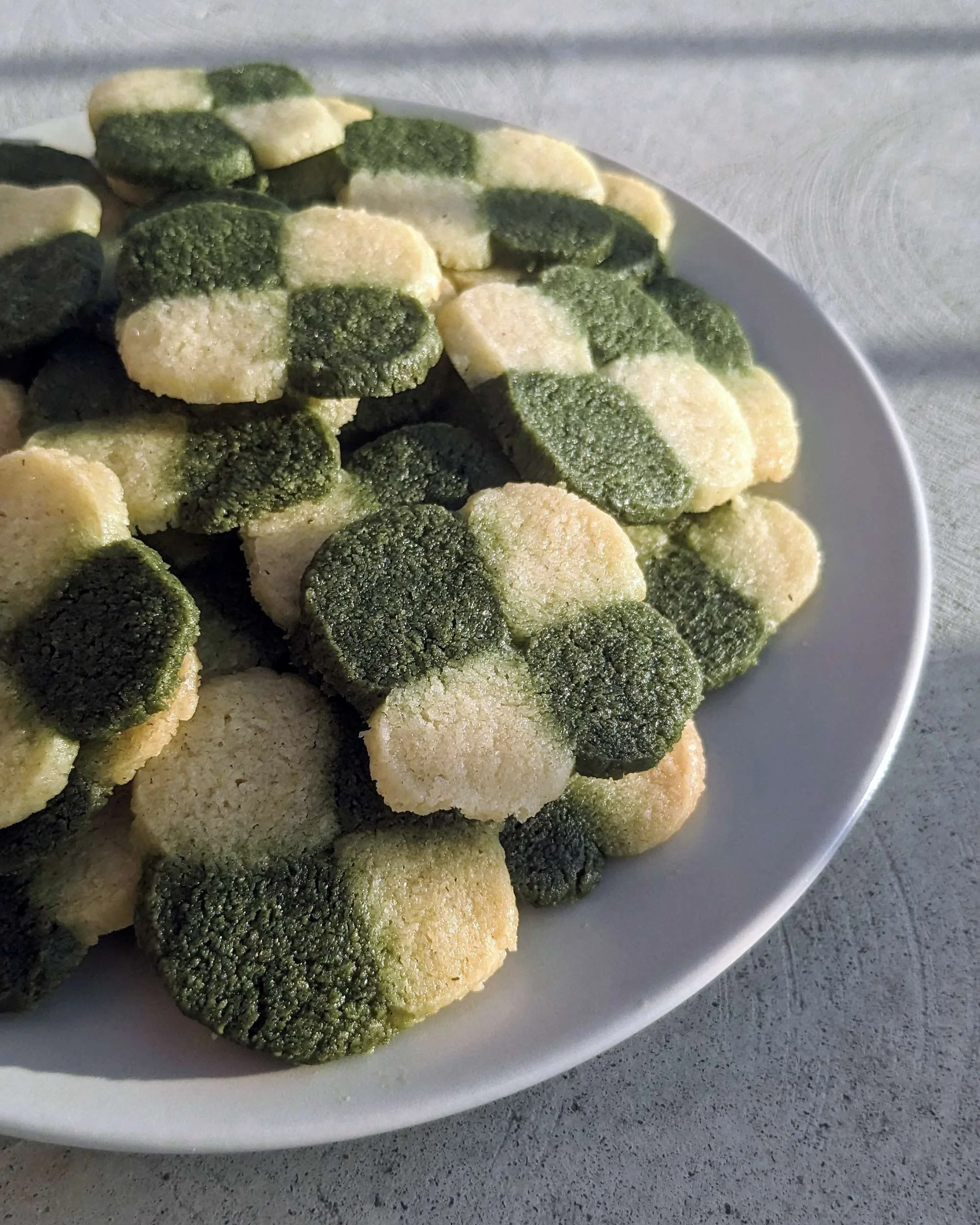 Biscuits sablés bicolores au thé matcha formant un motif d'échiquier et de fleur.