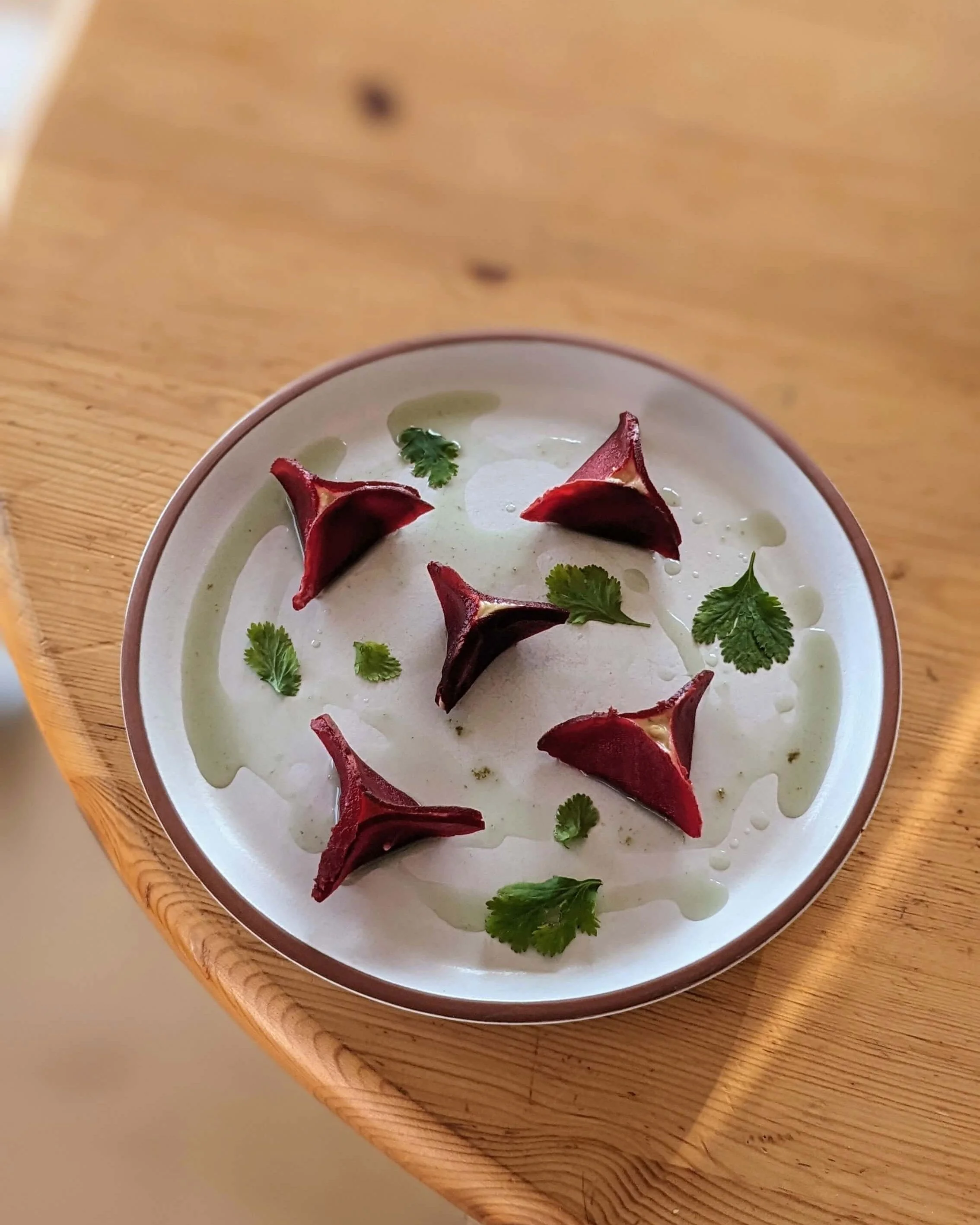 Ravioles de betterave triangulaires dressées avec soin, coriandre et huile d’herbes, illustrant une gastronomie bas carbone.