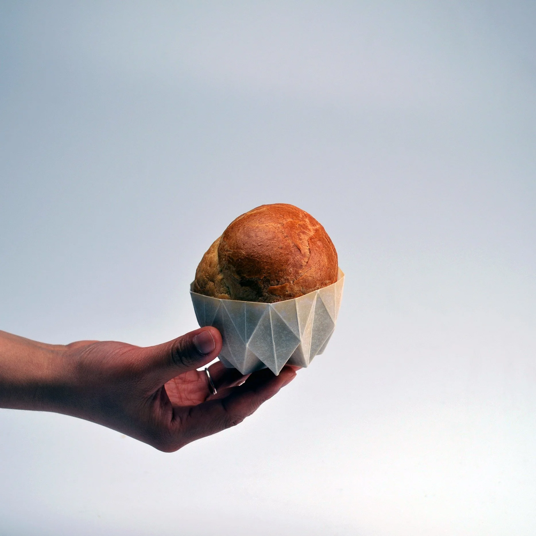 Main tenant une brioche cuite dans son moule en papier plié individuel.