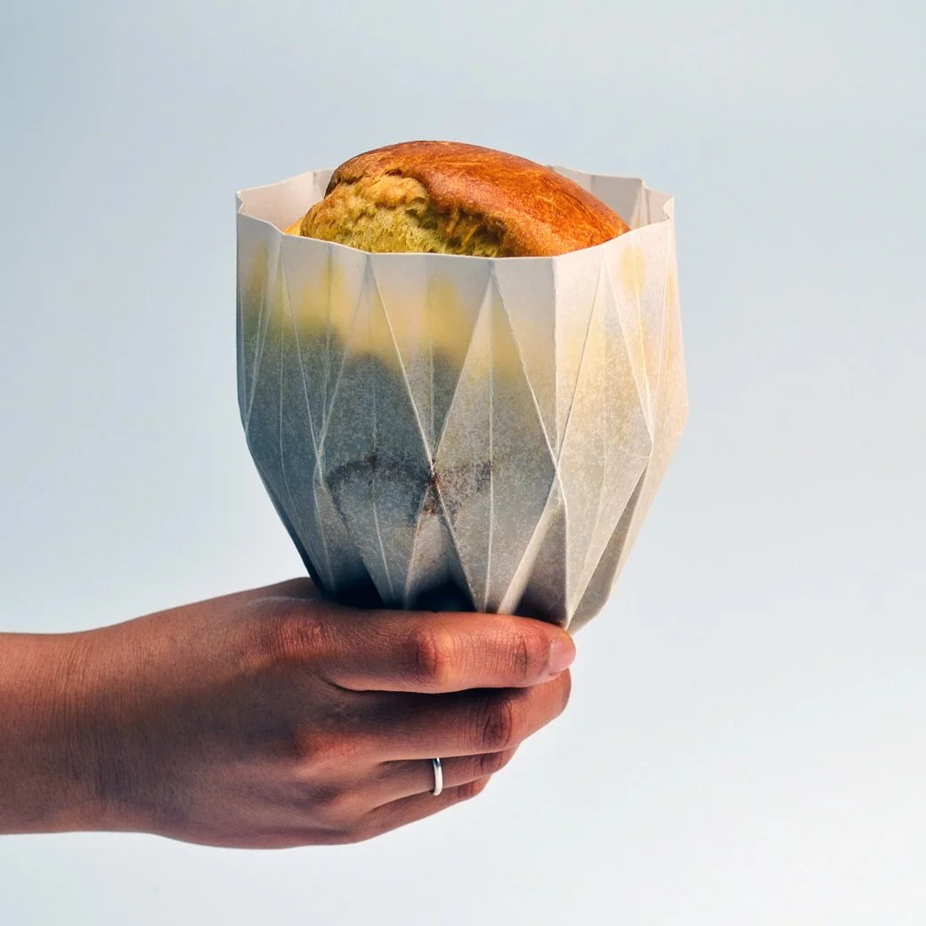 Main tenant une brioche allongée dans son écrin de papier.