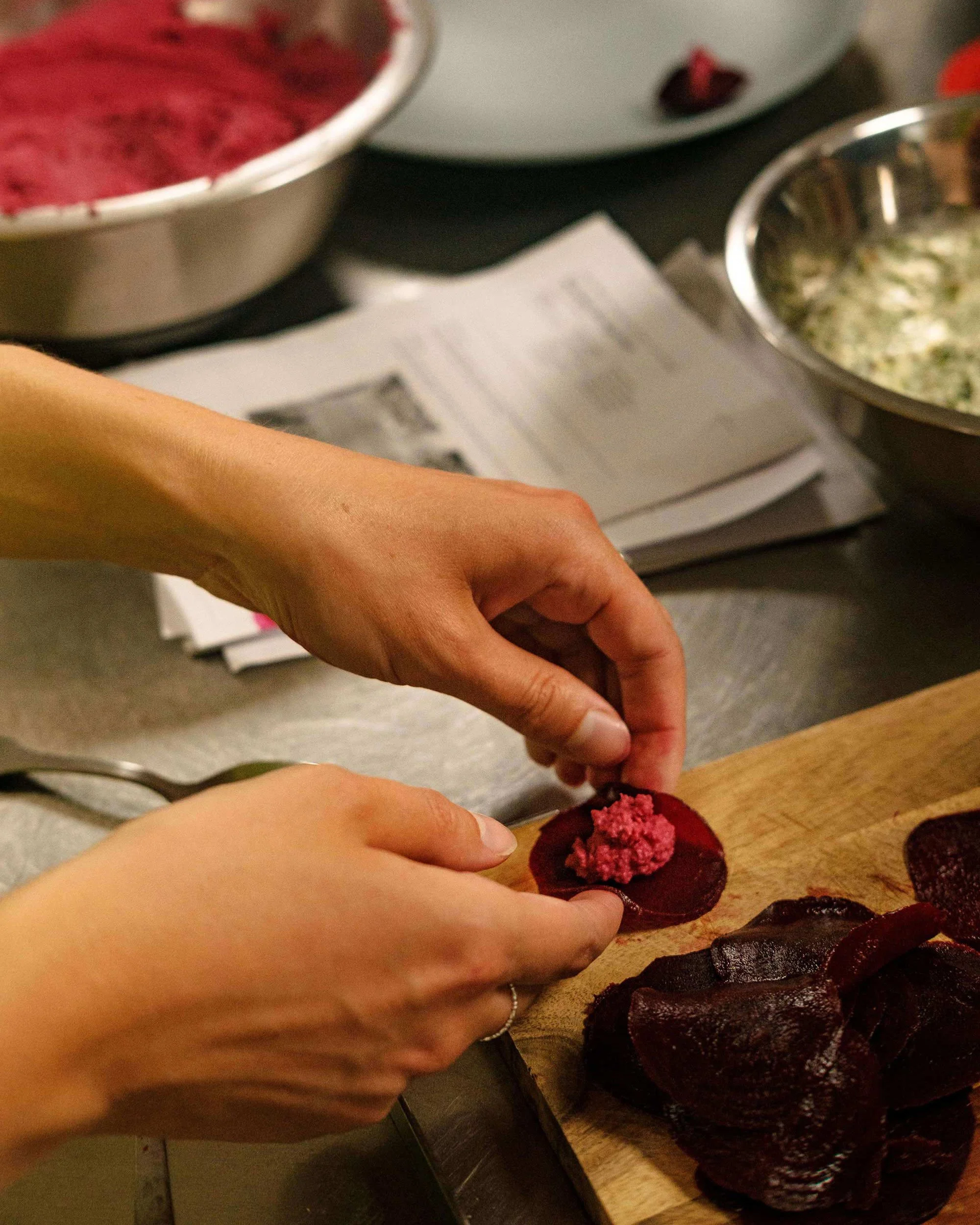 Gros plan sur des mains façonnant une raviole de betterave garnie de houmous lors d'un workshop de design culinaire.