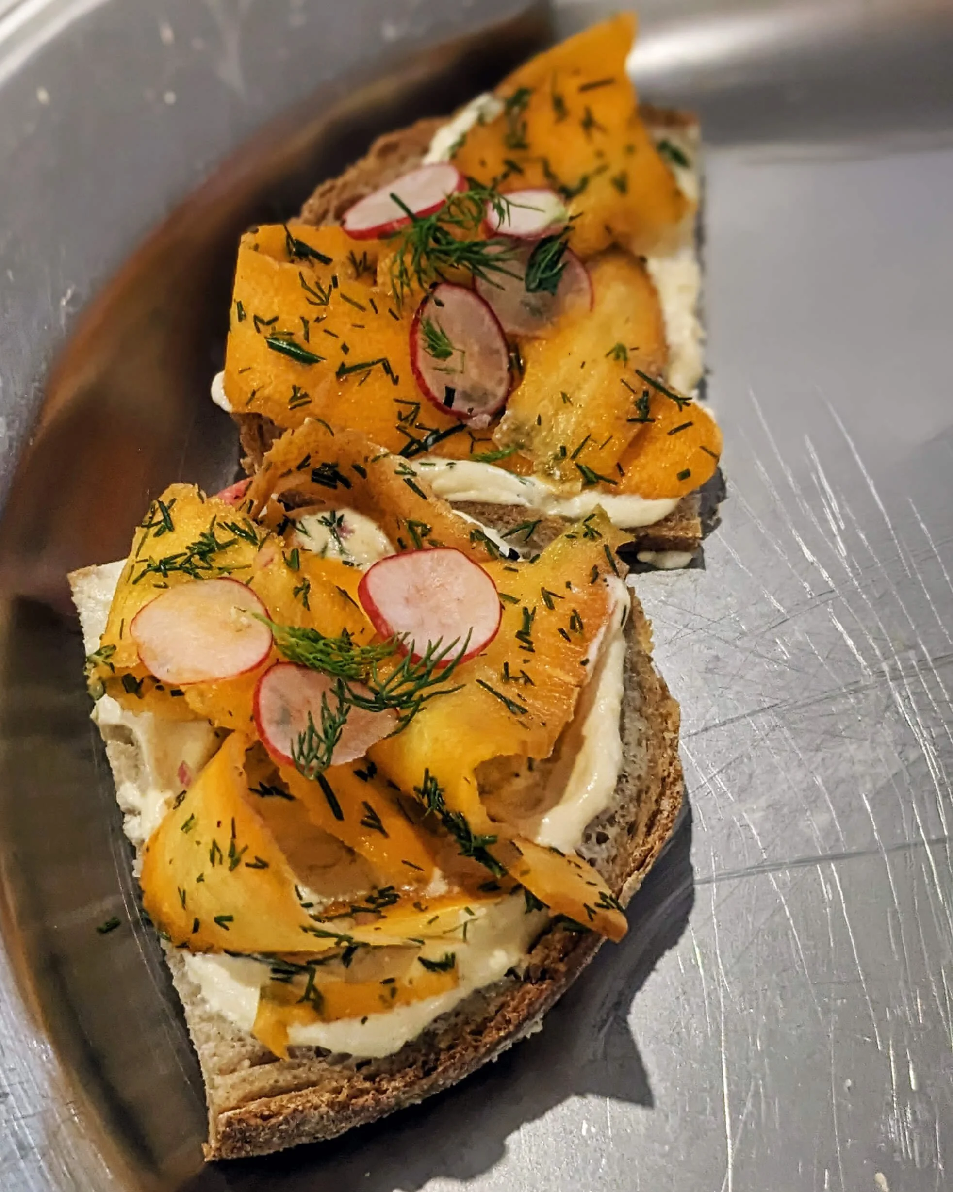 Toasts de gravlax de carottes à l’aneth, radis et crème de fromage frais à la moutarde, une création culinaire durable.