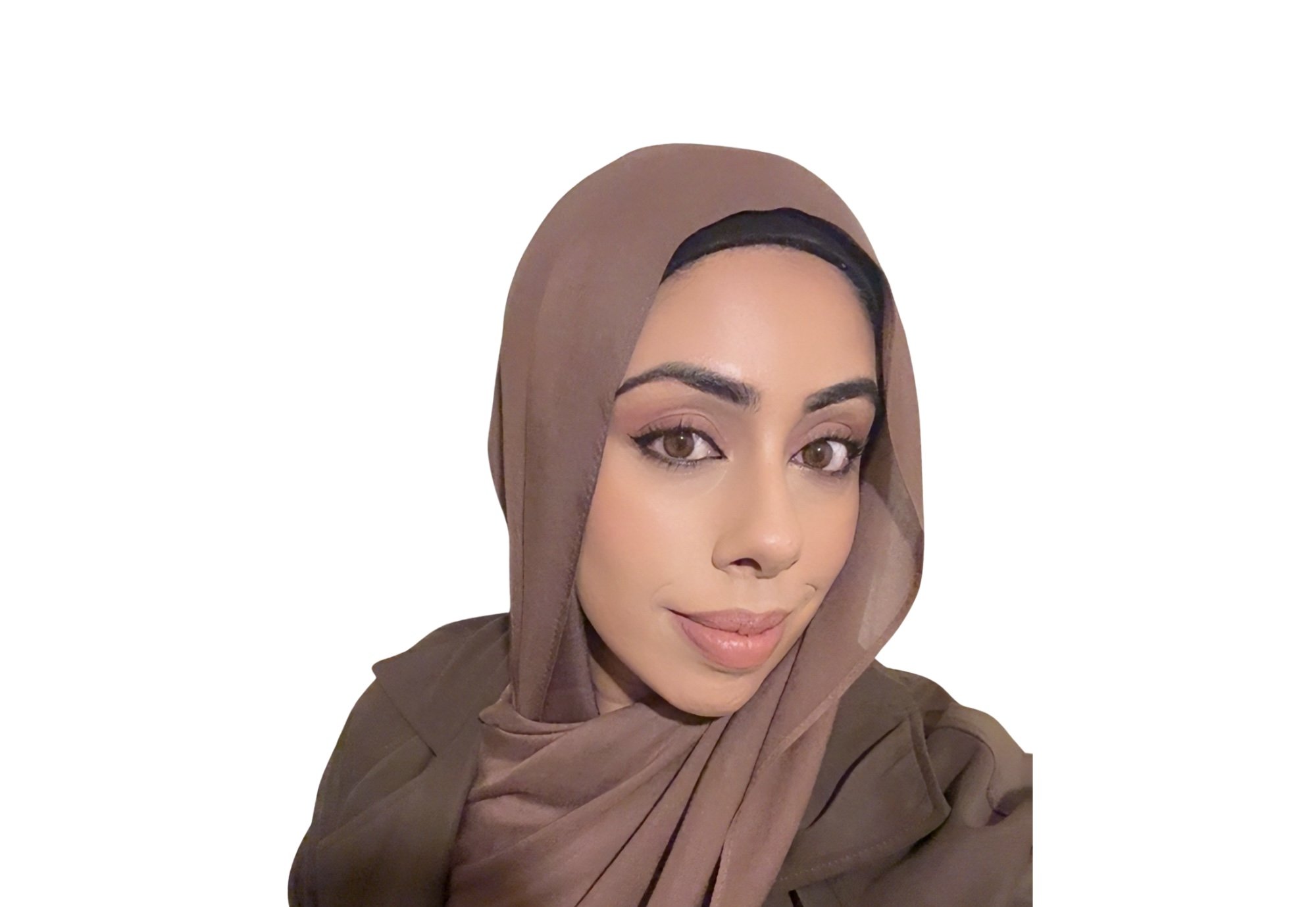 A woman wearing a brown hijab and matching brown outfit, taking a selfie inside a house near a door with glass panels.