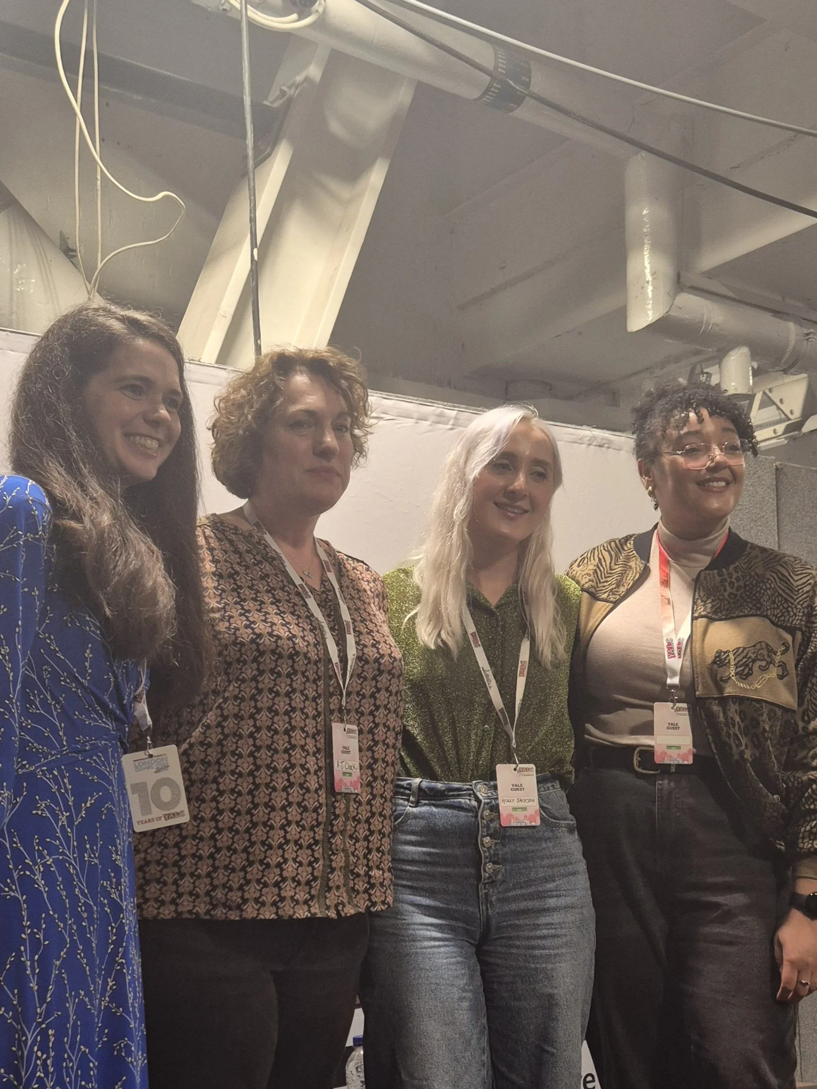 Four women standing side by side in a conference setting, wearing event badges, smiling and facing the camera.