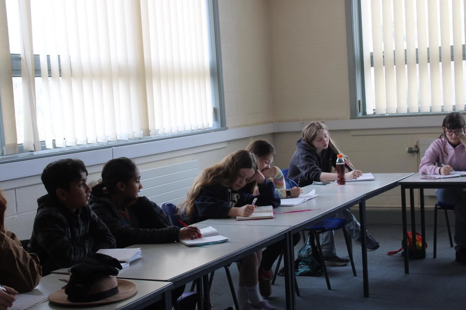 Students sitting at desks in a classroom taking notes and listening during a lesson.