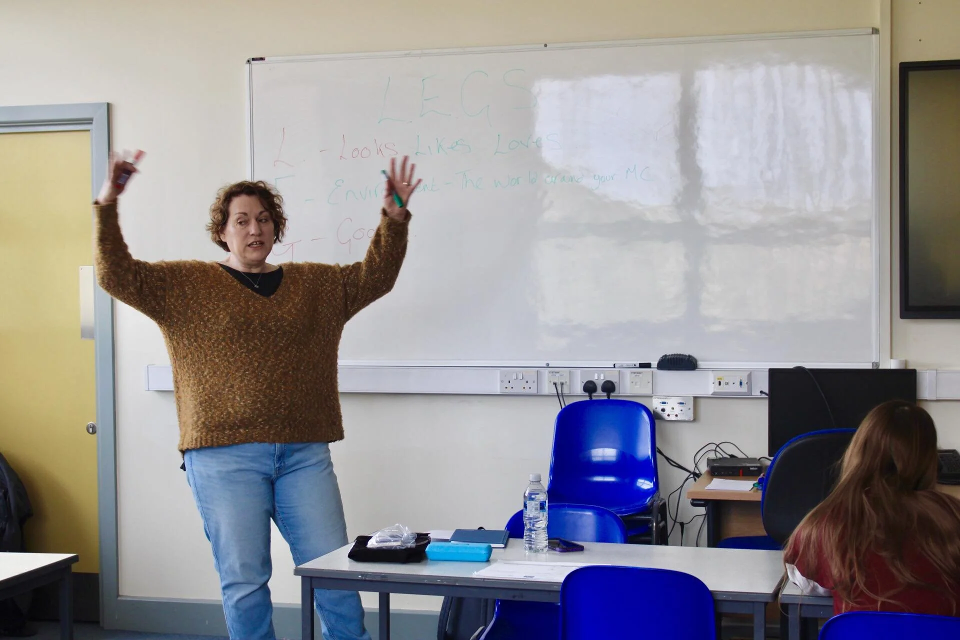 A woman standing in front of a whiteboard giving a presentation or lecture to a classroom of students.