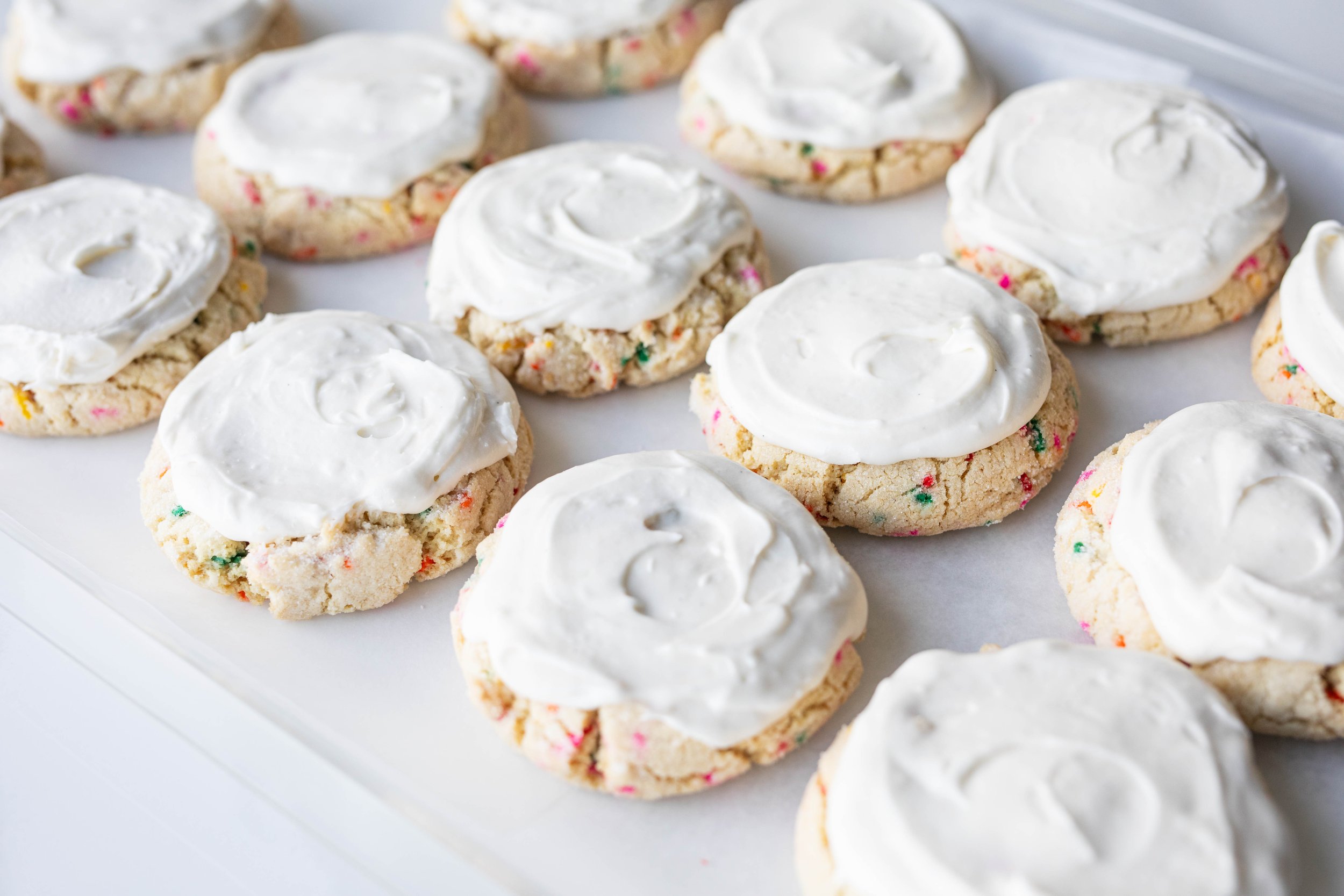 A tray of cookies with white frosting and colorful sprinkles.