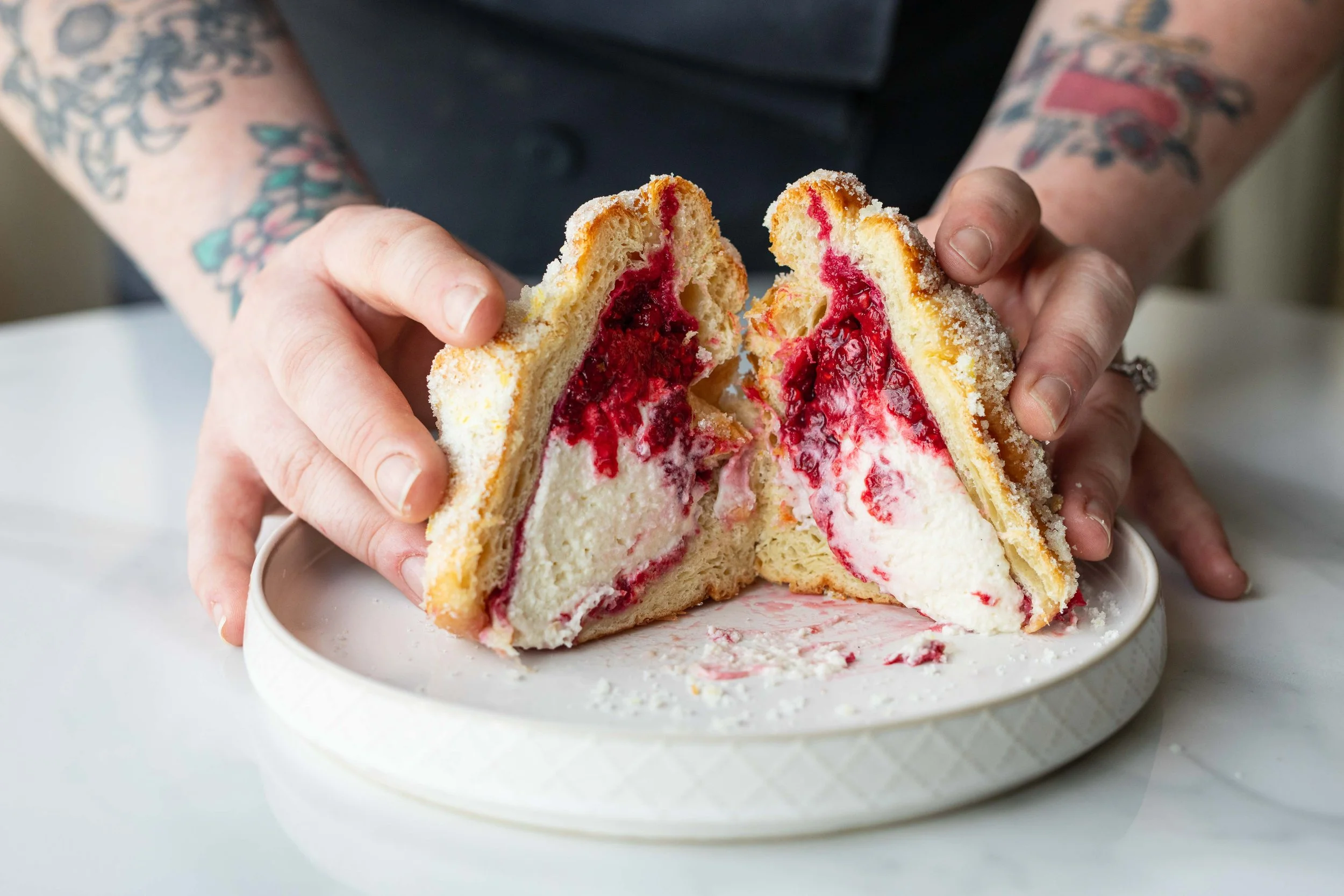 Person holding a sliced piece of white cake with red and purple berry filling and frosting, on a white plate.
