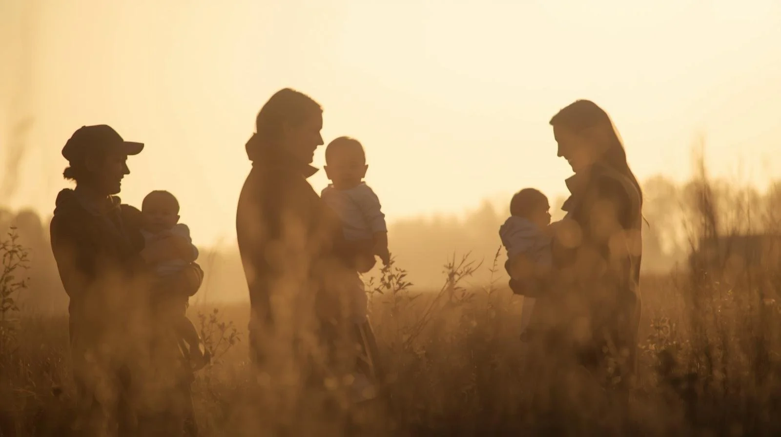 Silhouettes of two women and two children in a field during sunset.