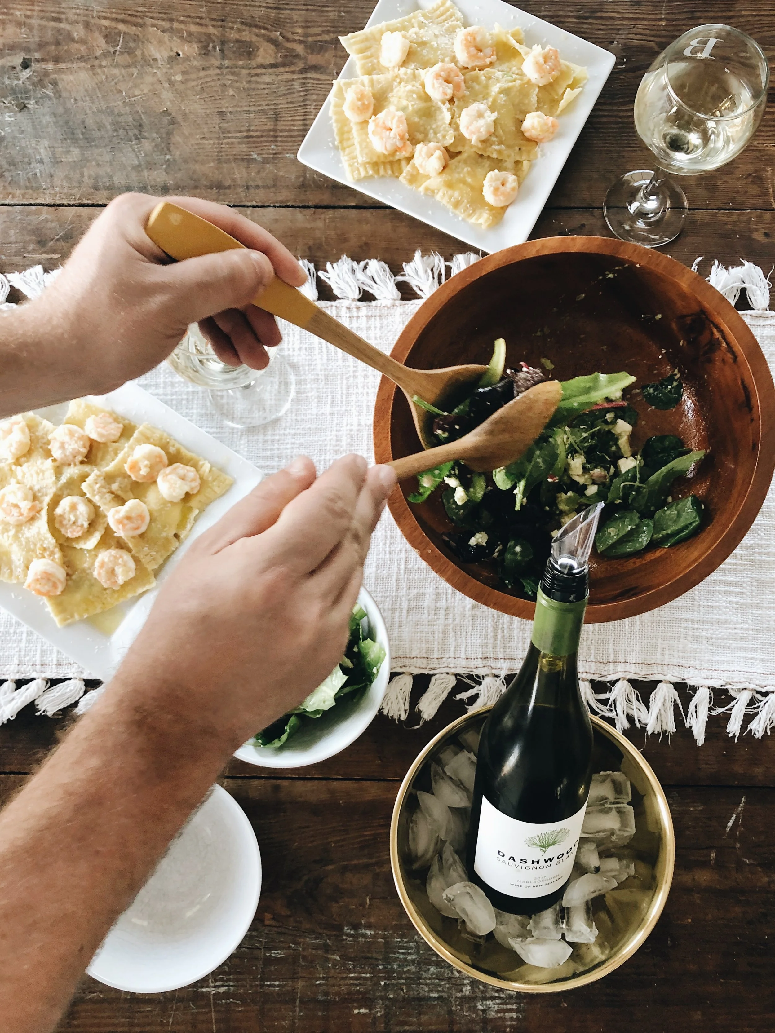 Gezonde salade en pasta met garnalen, witte wijn en een schaal met ijs op een houten tafel.
