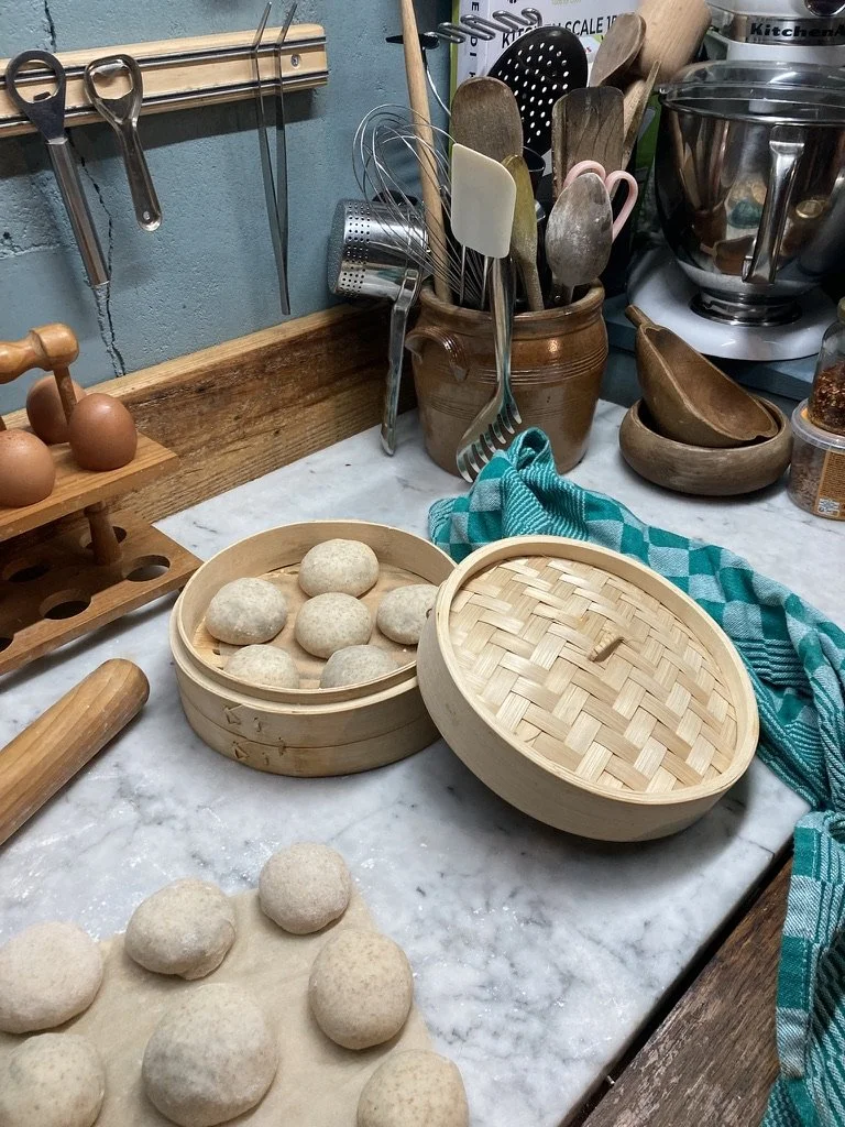 Marmer aanrecht met gestoomde deegballen in een ronde houten stoommandje, keukengerei en eieren in het achtergat.
