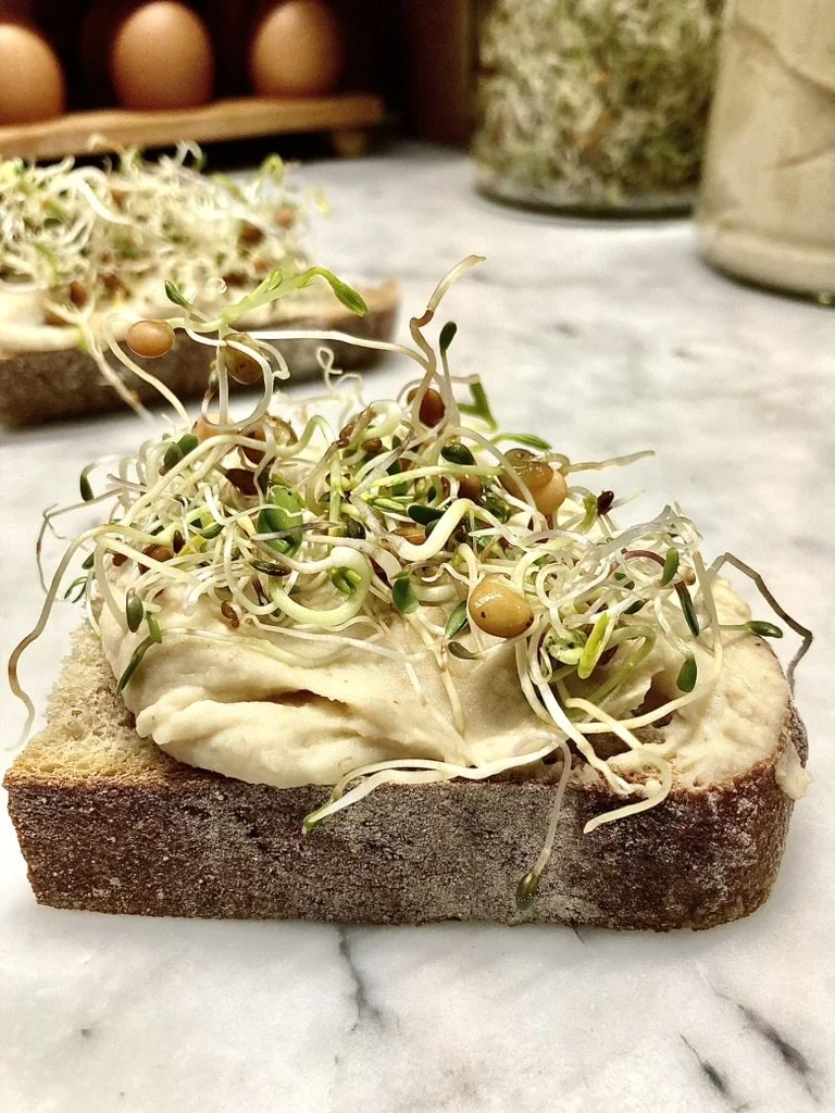 Een snee brood met hummus en een topping van sprouts.