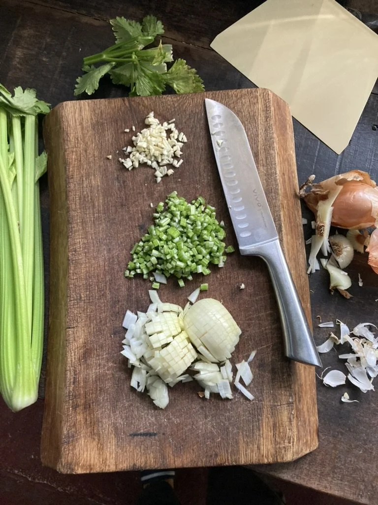 Snijplank met gehakte knoflook, gesneden groene uien, en gehakte sjalotten, naast een keukenmes