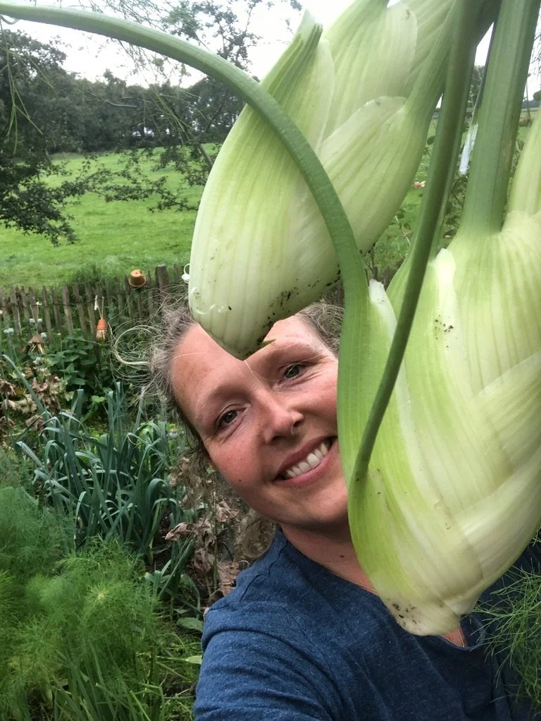 Een vrouw die in haar tuin staat en twee grote anjers vastheeft.