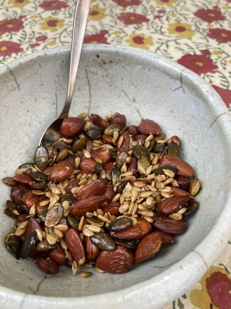 Een kom met gemengde zaden en noten op een bloemrijke tafelkleed.