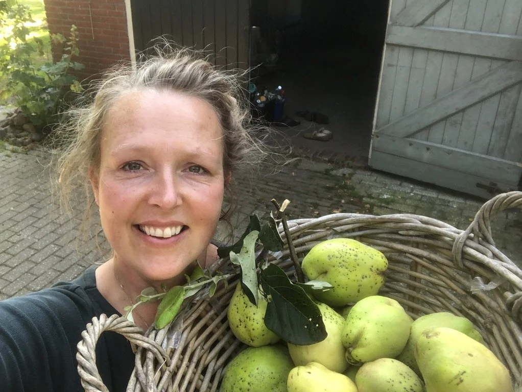 Een glimlachende vrouw houdt een mand met groene peren en een tak met bladeren.