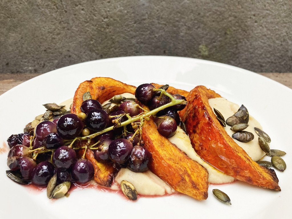 Gebakken zoete aardappelpartjes met blauwe bessen en pompoenpitten op een wit bord.