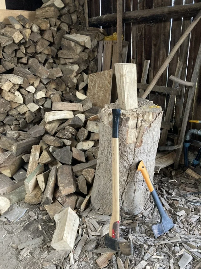 Stapel gezaagd hout en een grote boomstam in een houtwerkplaats, met twee hamers en een houten blok als werkoppervlak.