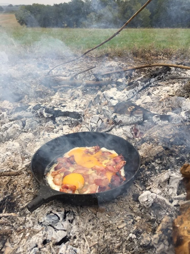Gemaakt eitje en spek in een pan boven een kampvuur in een open veld.