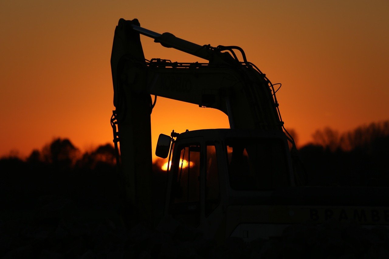 Silhouette of a construction excavator against a sunset or sunrise sky.
