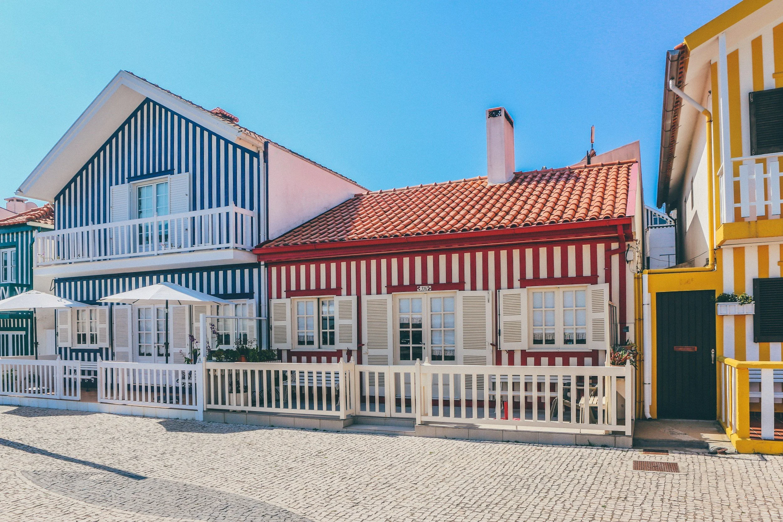 Colorful houses with striped facades and small balconies, set in a sunny outdoor area with cobblestone pavement.