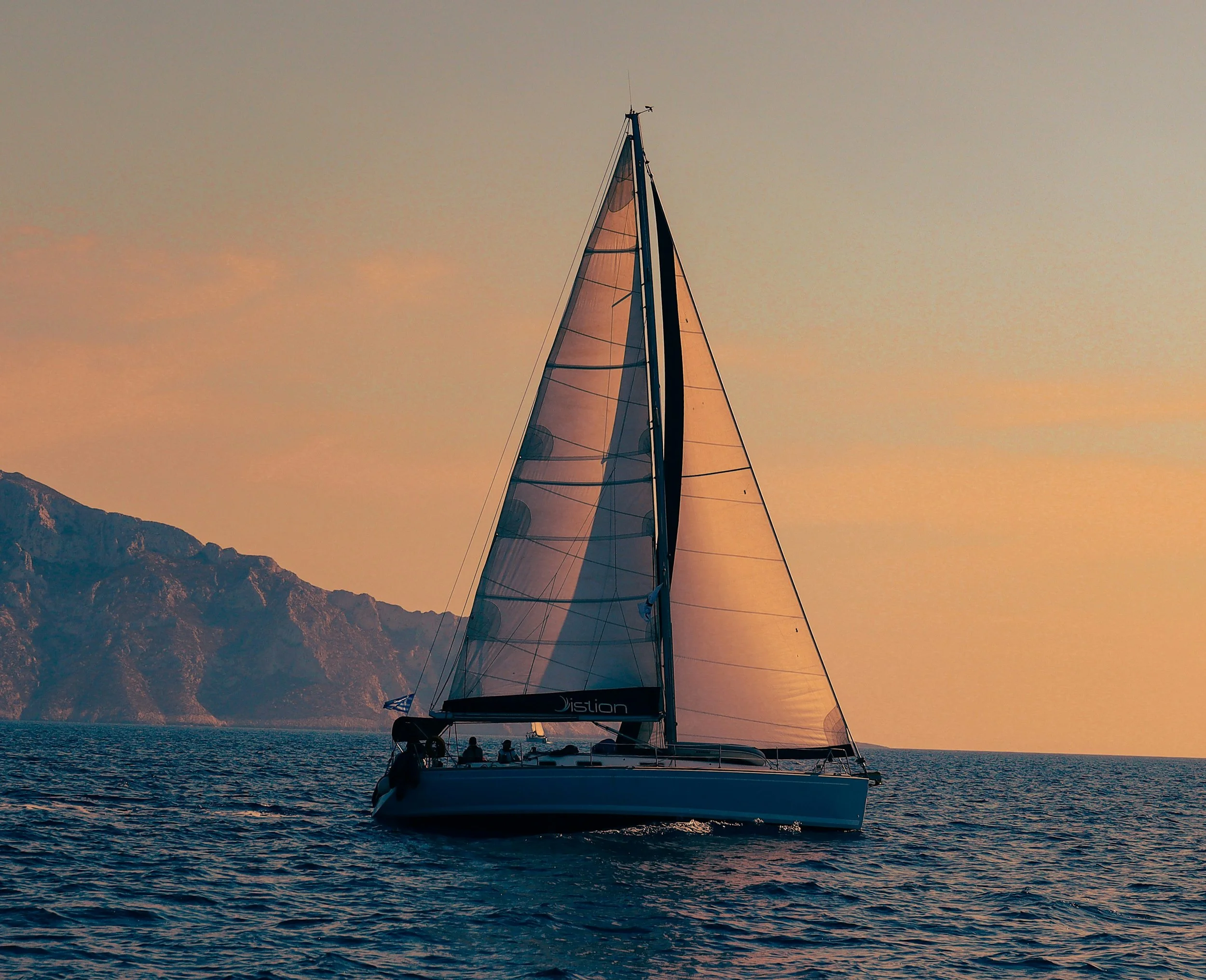 A sailboat on the water during sunset with mountain in the background.