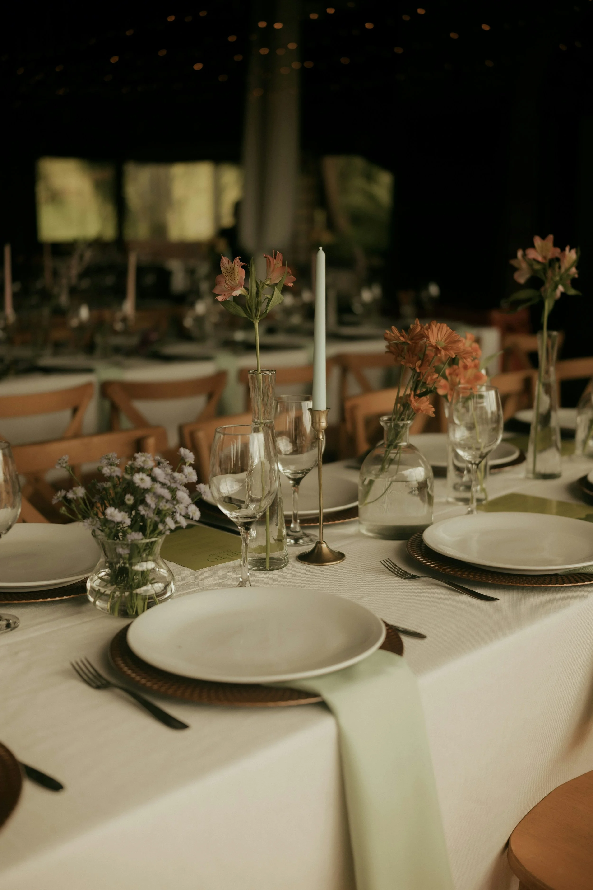 A banquet table decorated with floral arrangements in vases, white plates, wine glasses, and cutlery, set for a formal event.