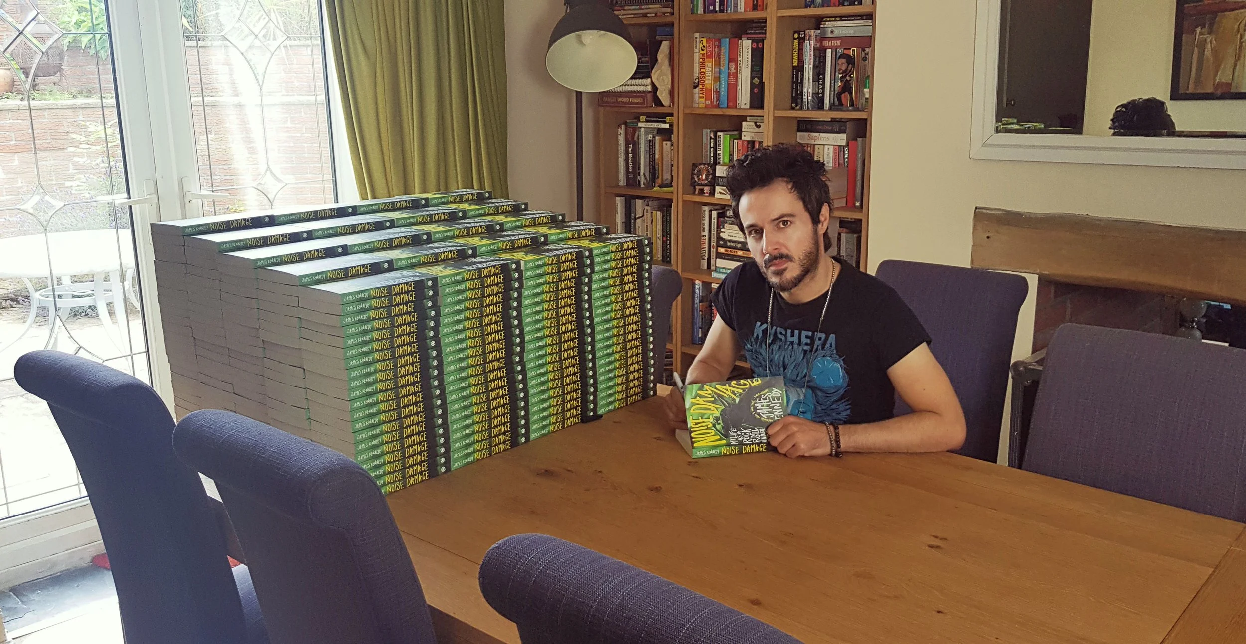 James Kennedy, the author of the books 'Noise Damage' and 'Loud Medicine' posing with a stack of his books