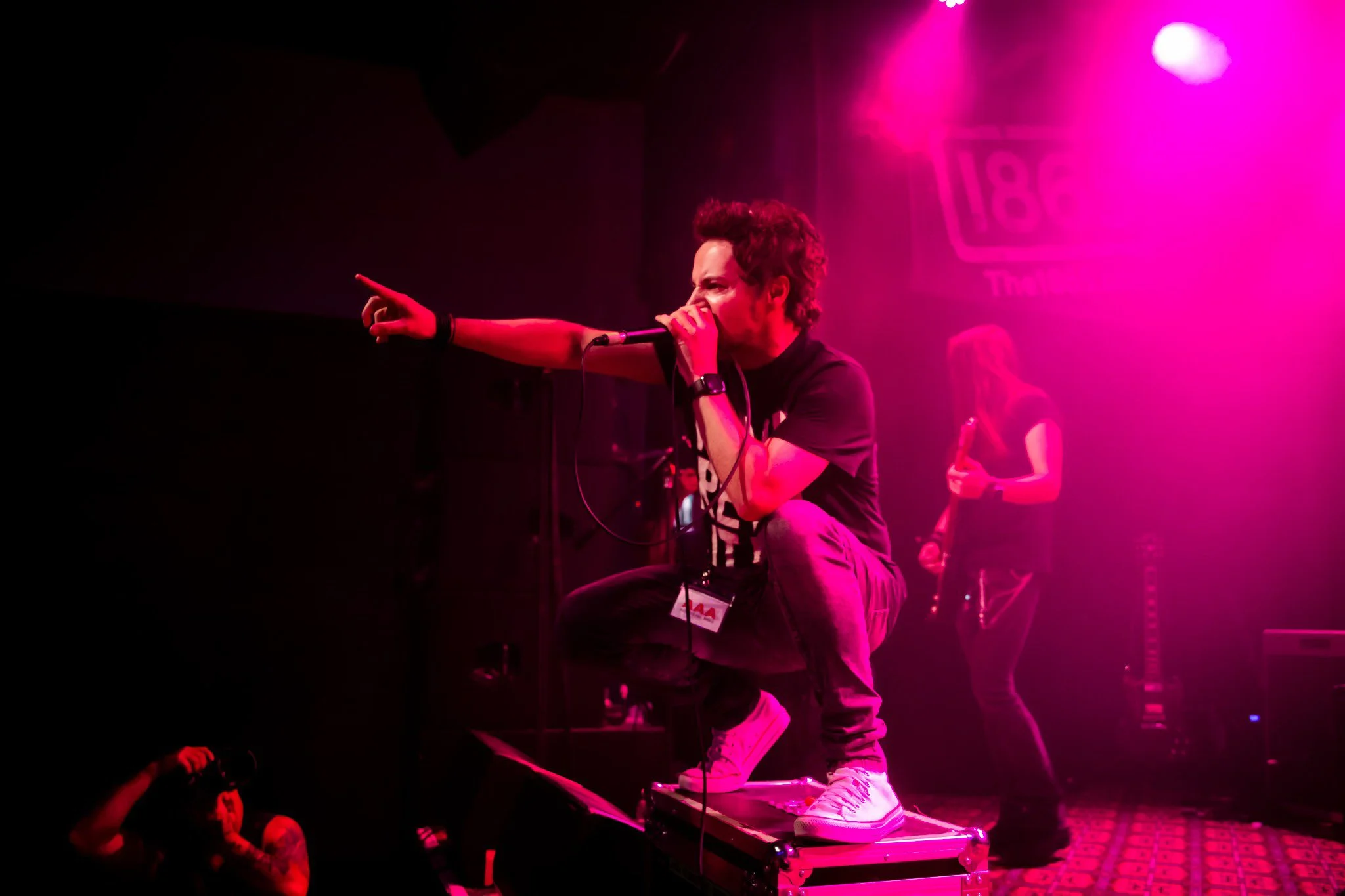 James Kennedy, the singer, author and podcaster from Wales performing live on stage with his hard rock band 'James Kennedy and The Underdogs', crouched down on his stage box under pink lights 