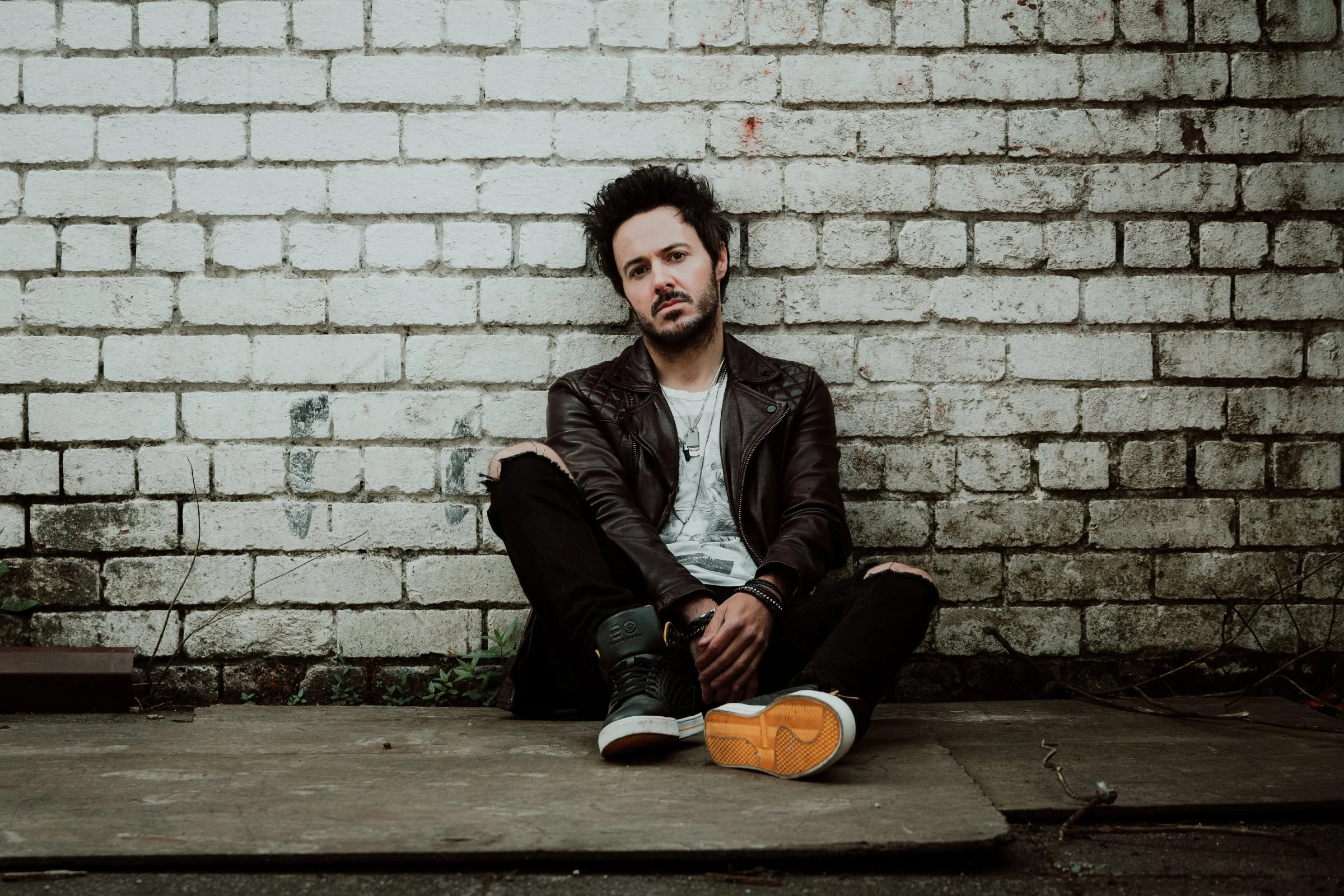 James Kennedy, singer in the Welsh rock band 'James Kennedy and The Underdogs' sitting on the floor for a photoshoot against a white, dirty wall 