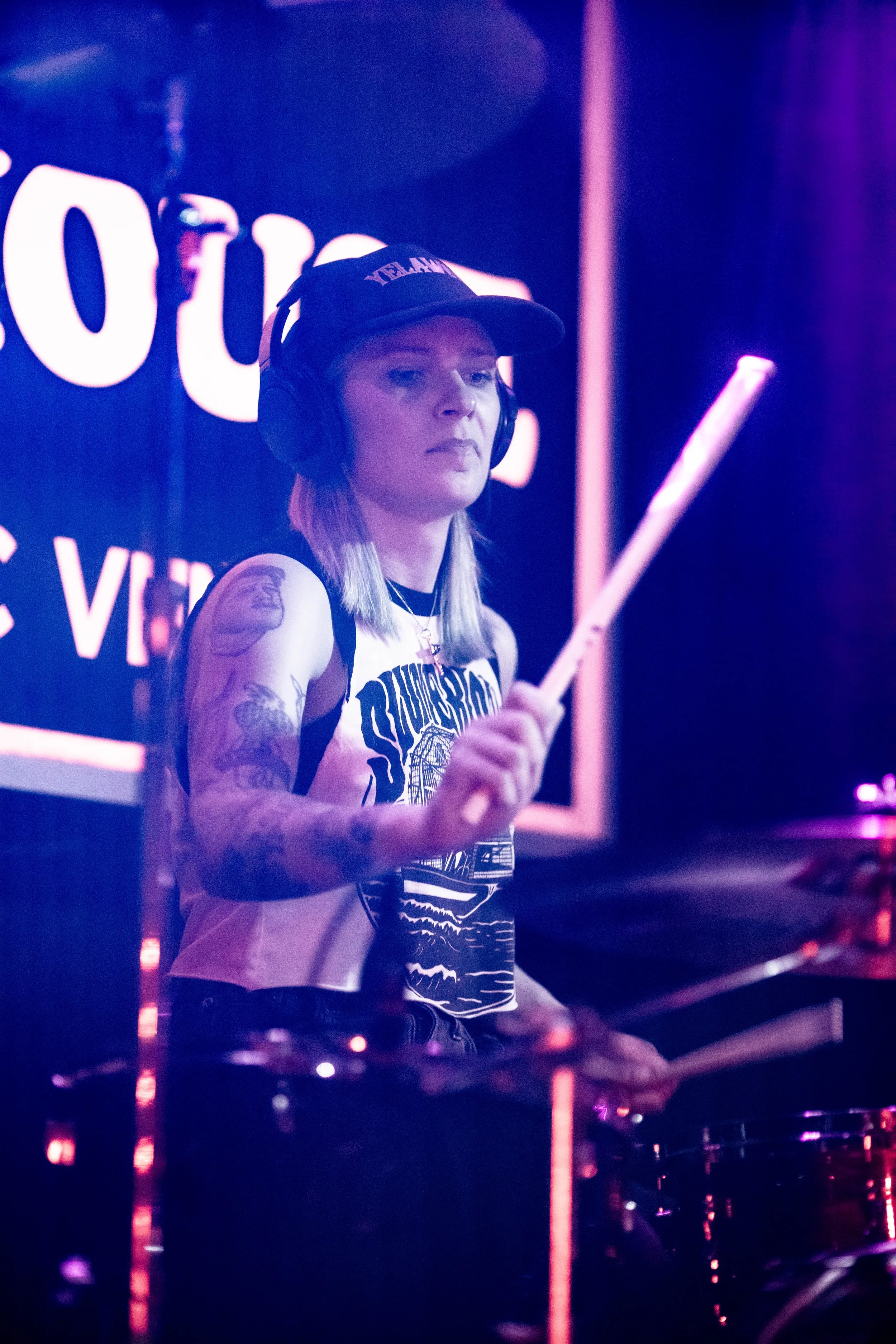 Aggy Nowicka, the female drummer in the UK hard rock band 'James Kennedy and The Underdogs', on stage playing drums wearing a cap under purple stage lights 