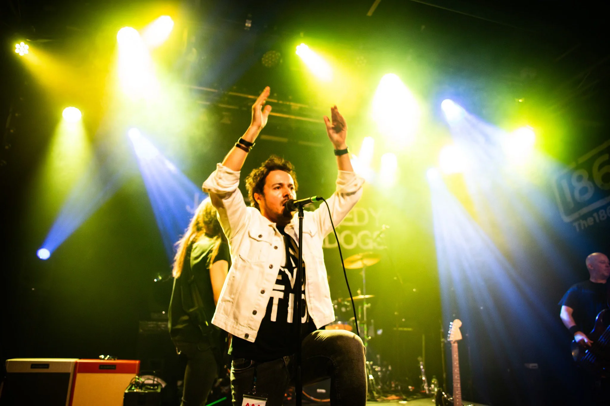 'James Kennedy and The Underdogs', the hard rock band from Wales UK performing live on stage under yellow stage lights with the singer, James Kennedy clapping his hands