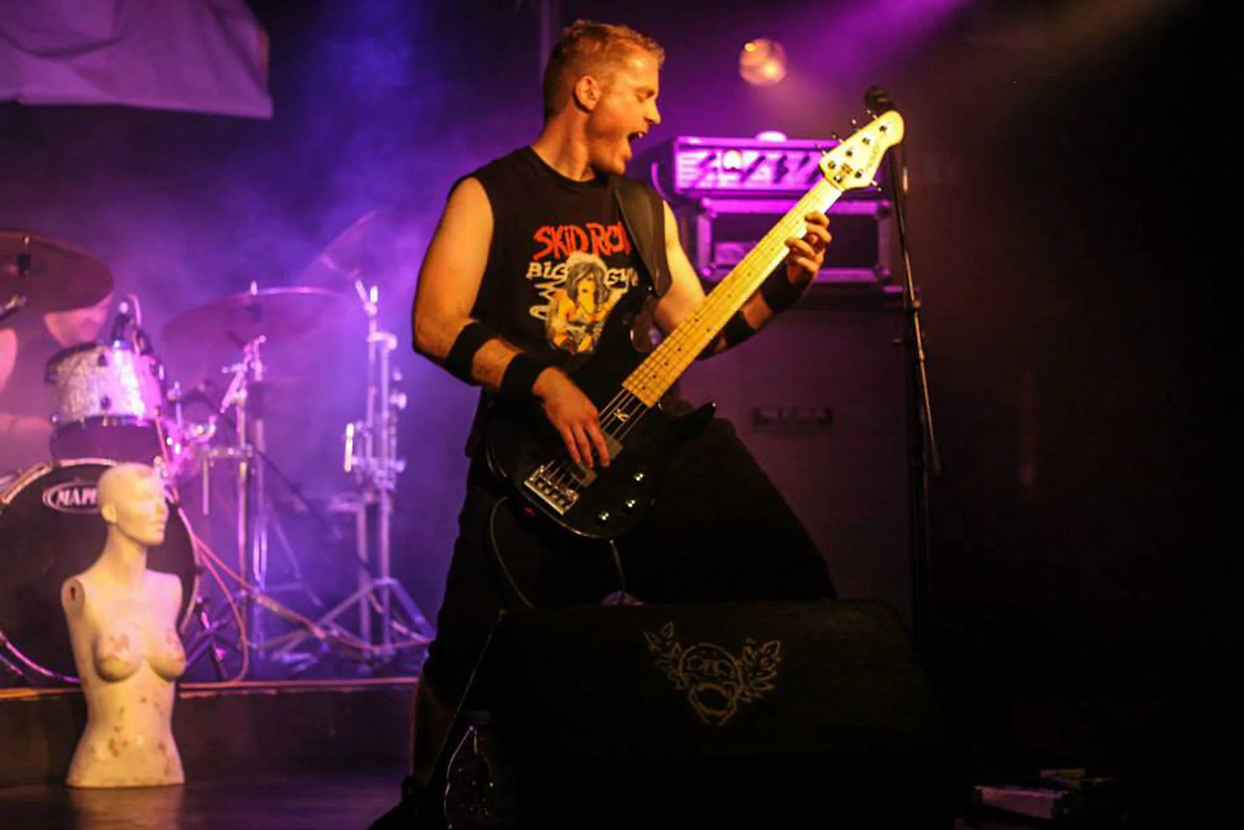 Kyshera bassist, Matt Warr playing bass at a Kyshera concert in Milton Keynes in purple stage lights with stage mannequin