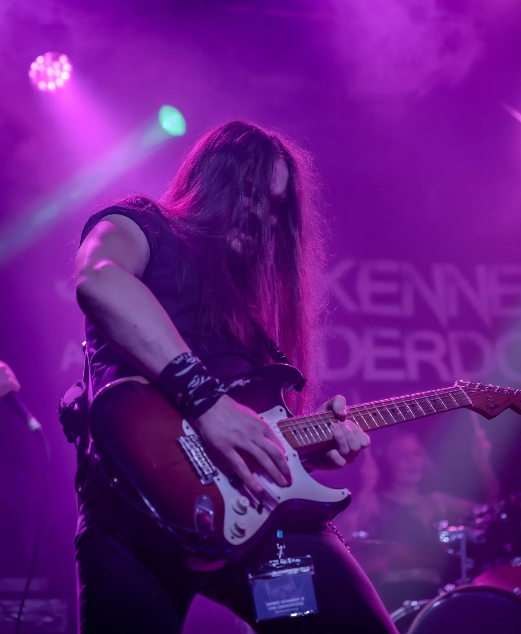 Jack Davies, lead guitarist with the rock band 'James Kennedy and The Underdogs' playing a guitar solo and bending the guitar strings during a concert under purple stage lights