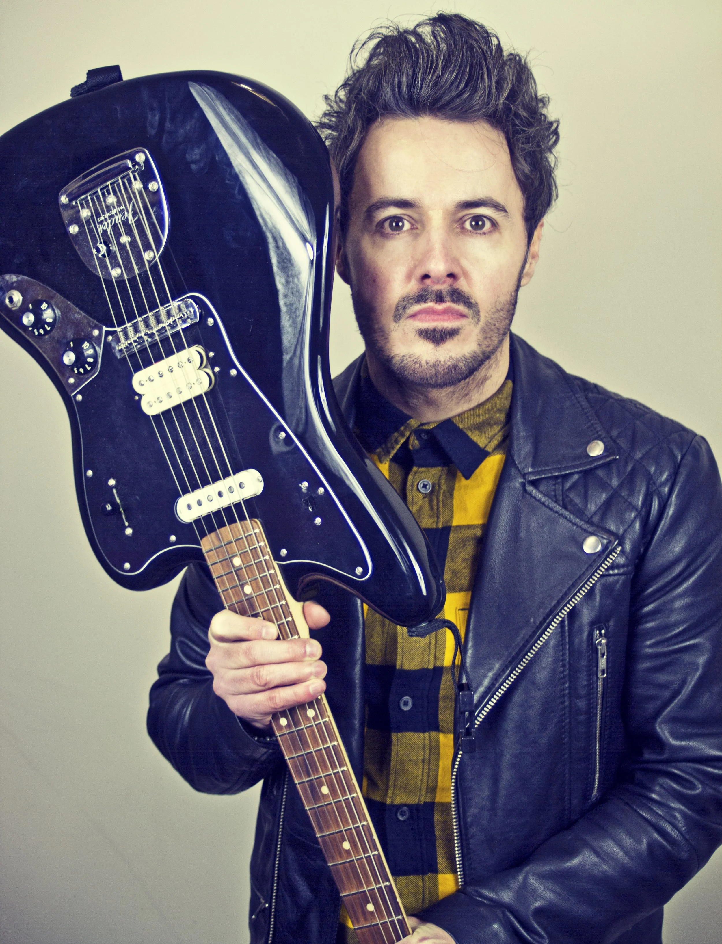 James Kennedy, the singer, author and frontman in the band, James Kennedy and the Underdogs posing with his Fender Jaguar guitar, a leather jacket and checkered shirt