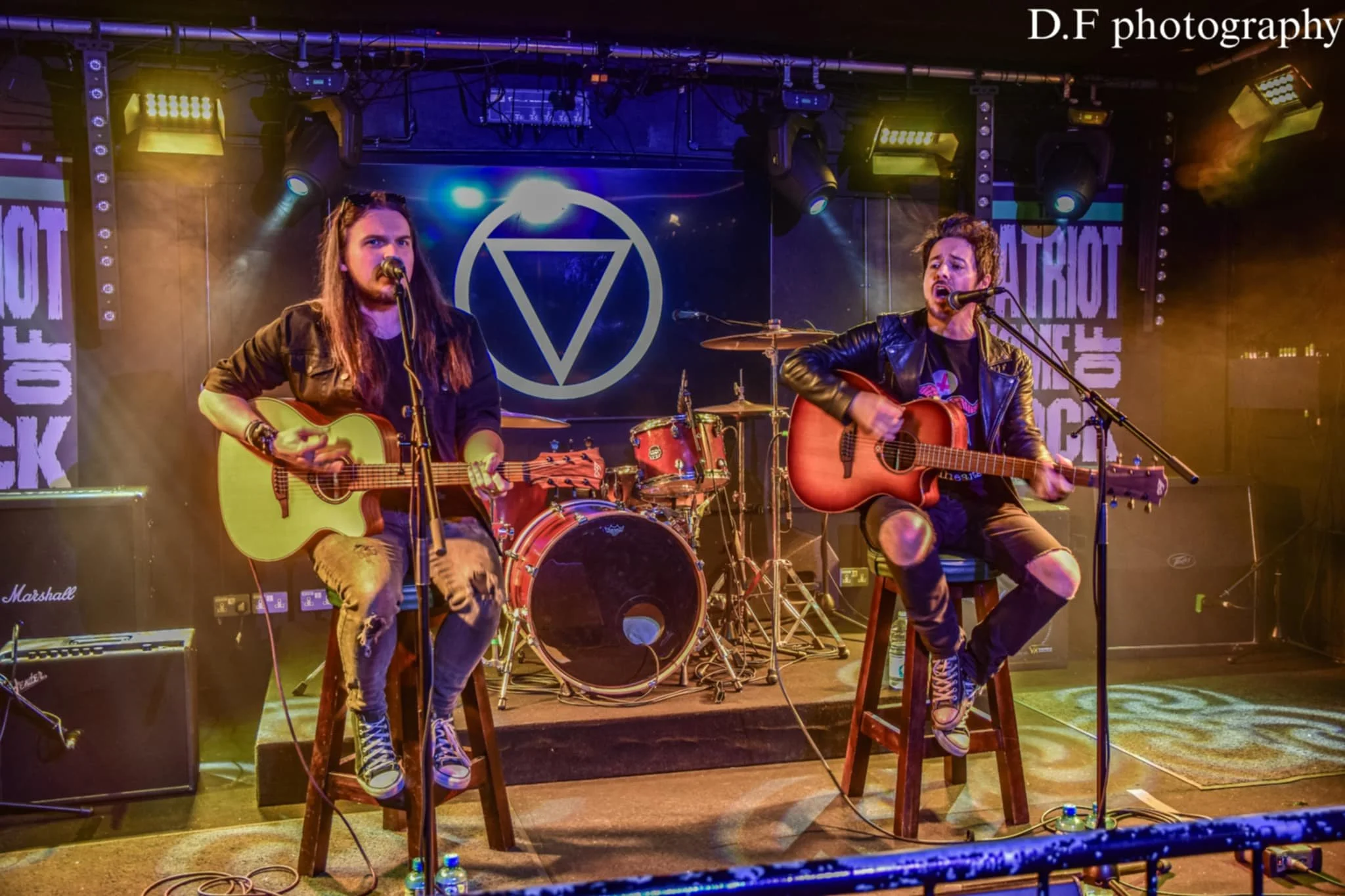 Jack Davies and James Kennedy from the band 'James Kennedy and The Underdogs' performing an acoustic duo gig together, sat on stools and playing acoustic guitars 
