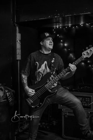 Elliot Blake, the bass player in the Welsh punk band 'James Kennedy and The Underdogs' live on stage wearing a baseball cap and playing his bass