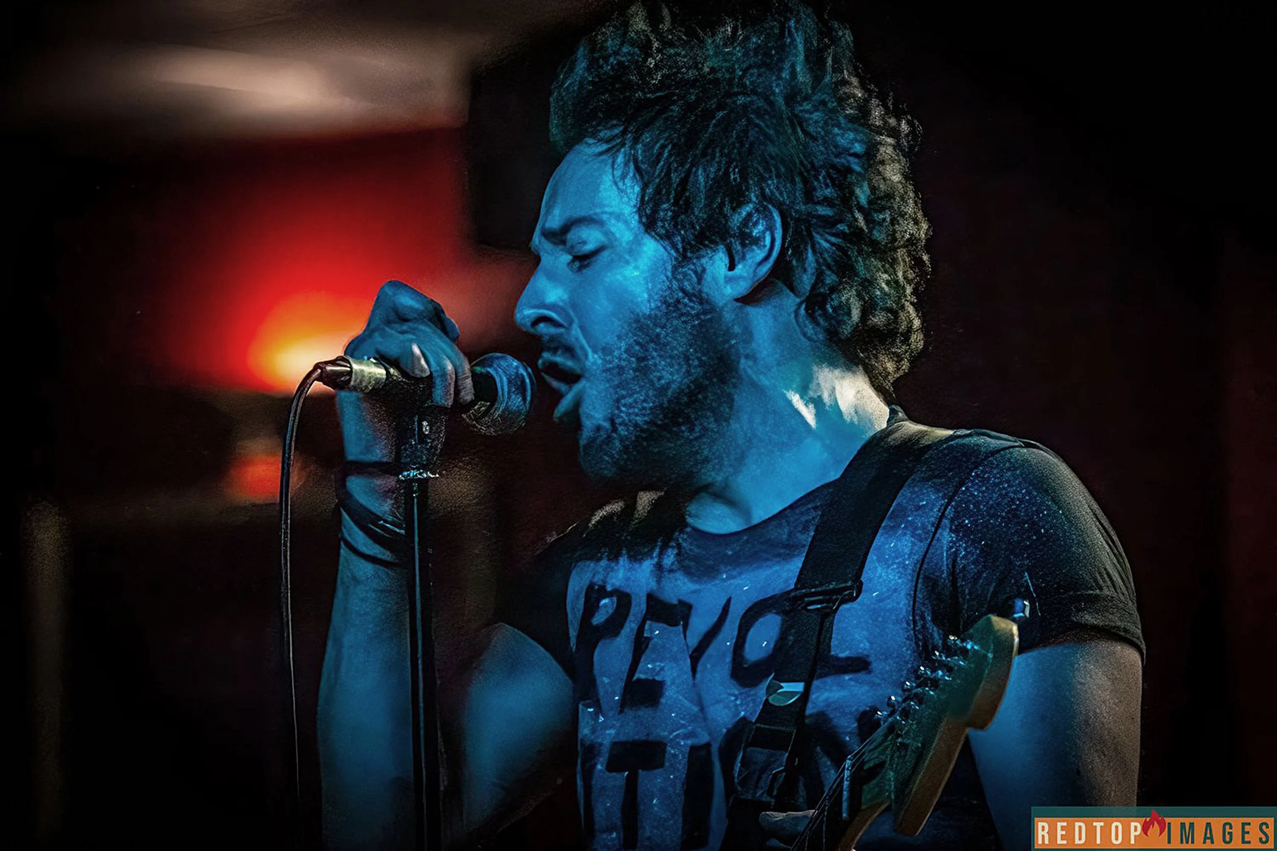 James Kennedy, the singer, author and podcaster singing on stage with his punk rock band 'James Kennedy and The Underdogs' wearing a spray painted t-shirt that says Revolution